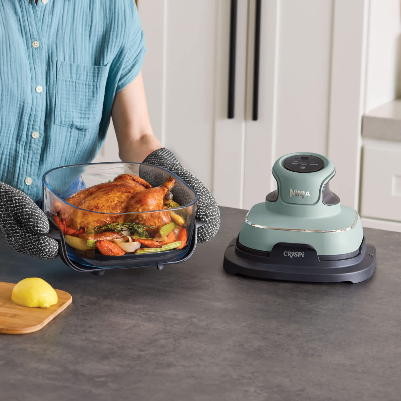 Personne tenant le r&eacute;cipient en verre Ninja Crispi contenant un poulet entier et des l&eacute;gumes