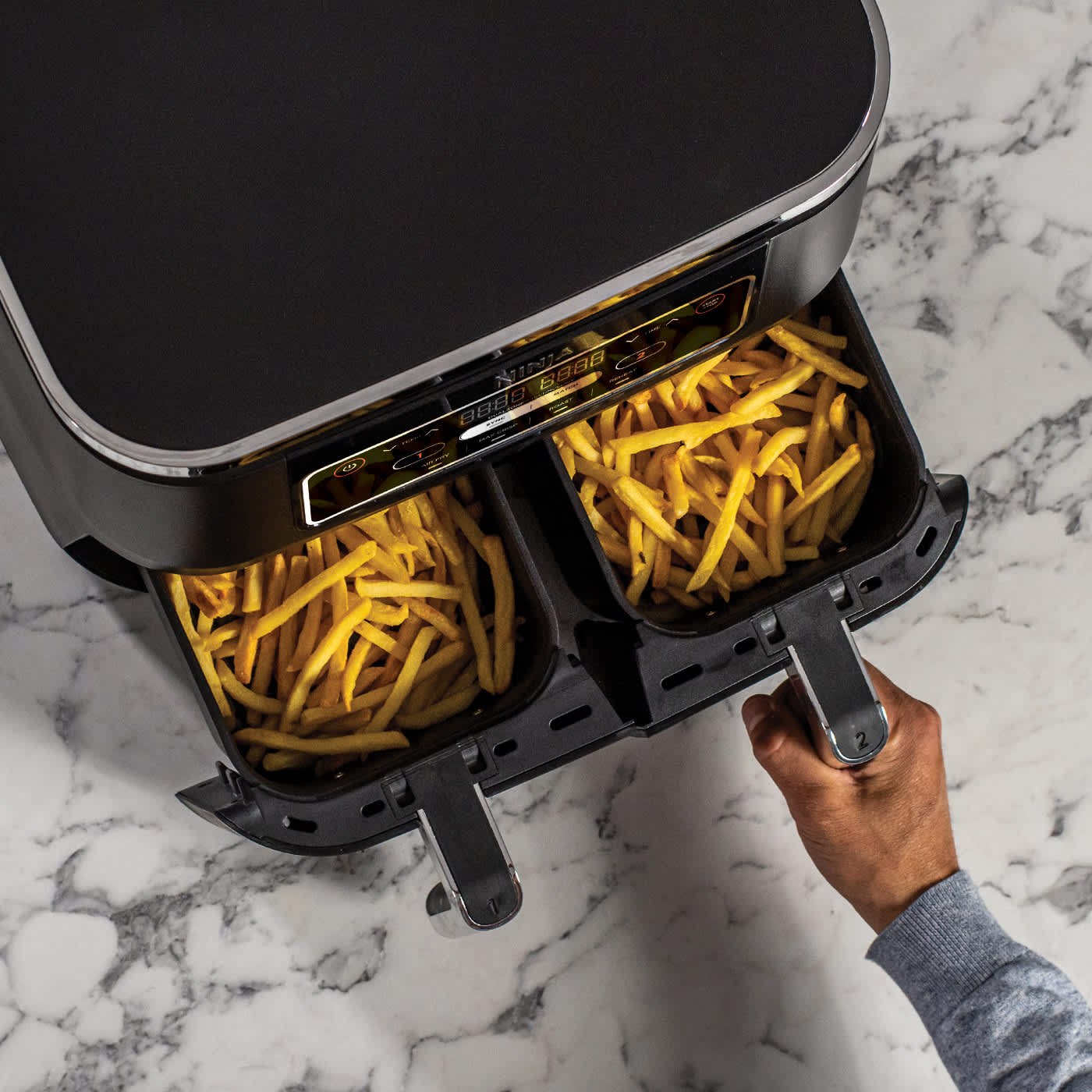 Airfryer avec tiroirs remplis de frites, une personne ouvrant l&rsquo;un des tiroirs.