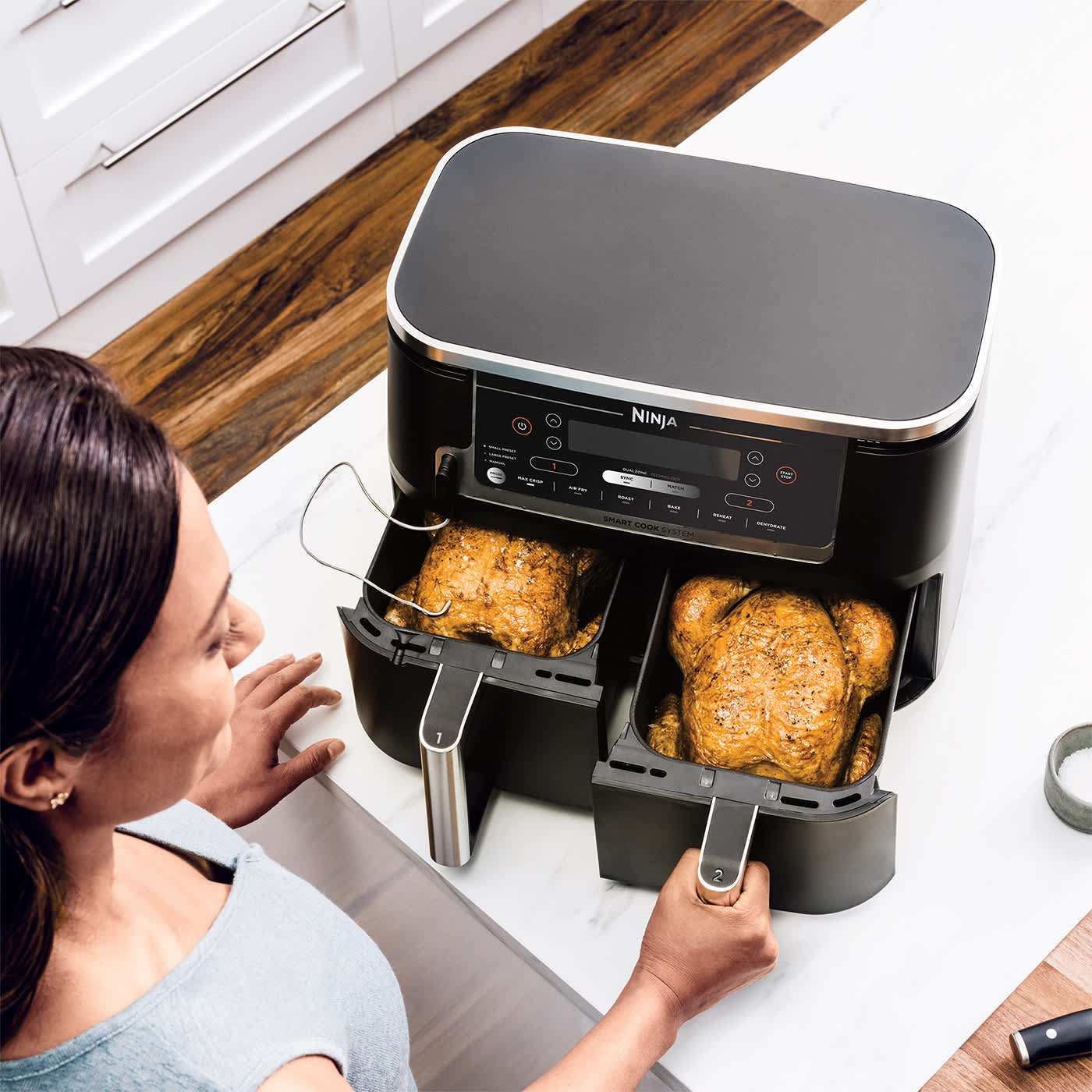 Femme ouvrant les deux tiroirs du ninja air fryer contenant des poulets entiers.
