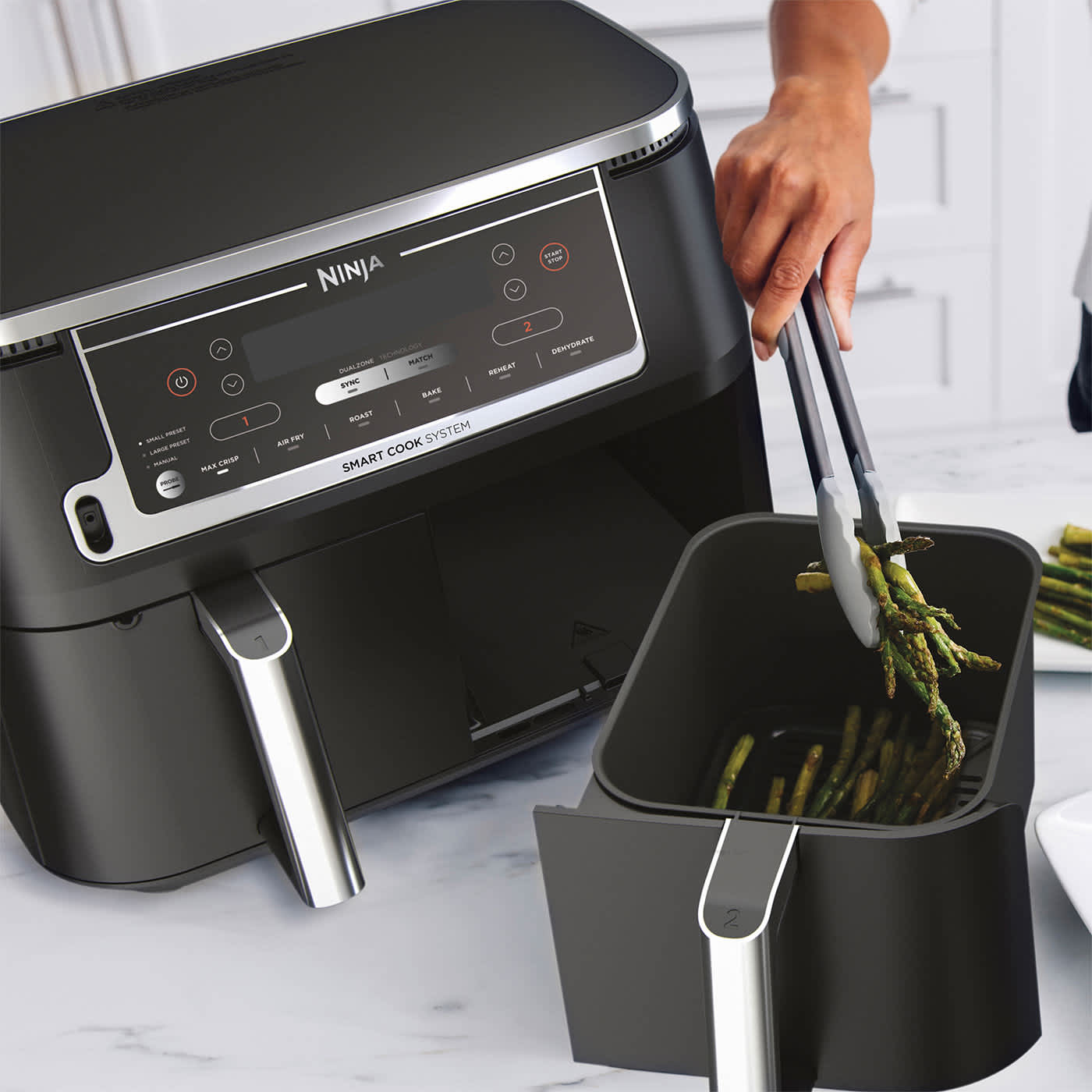 Personne utilisant des pinces pour sortir des asperges du tiroir de l'air fryer.