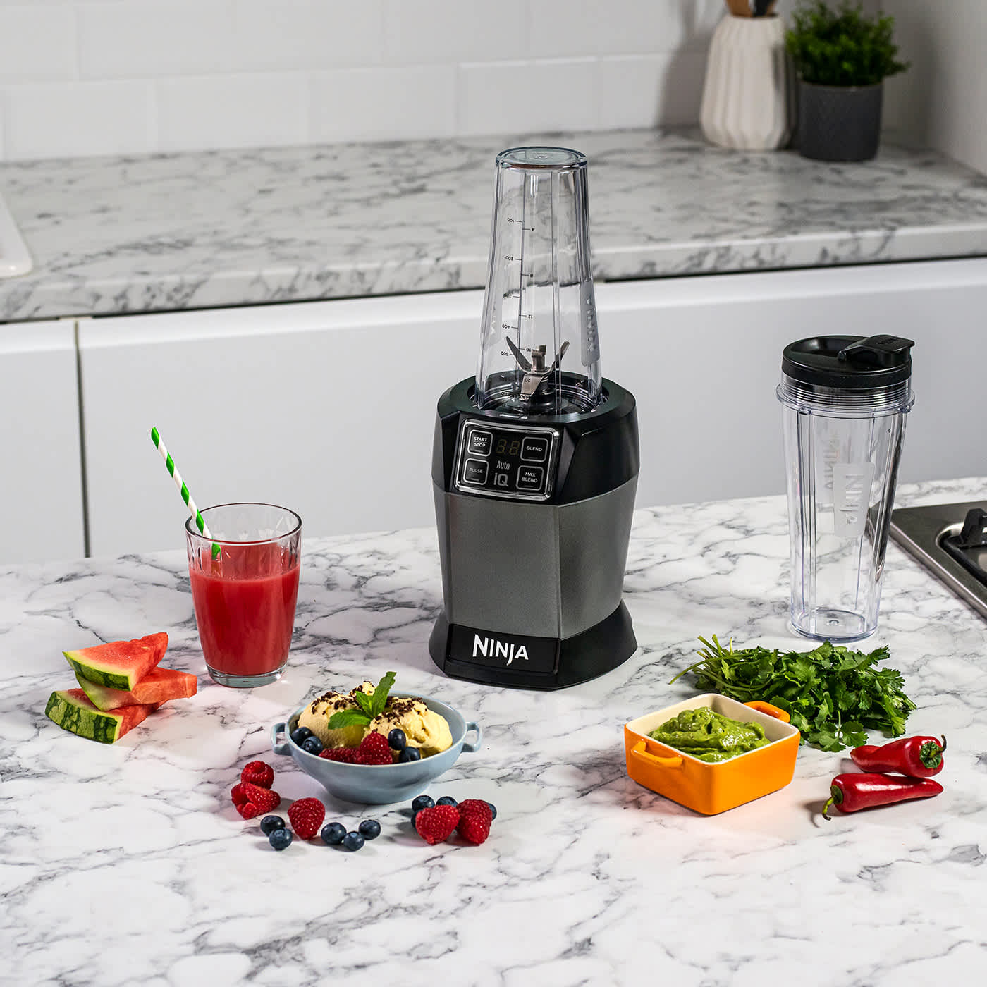 Blender sur une table avec un smoothie, un bol de smoothie et des l&eacute;gumes.