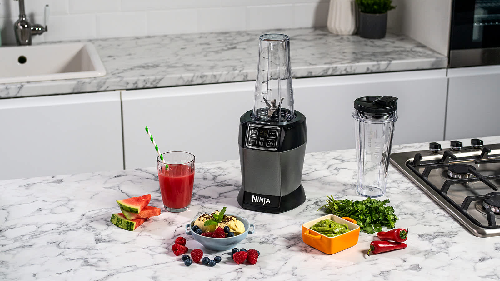 Blender sur une table avec un smoothie, un bol de smoothie et des l&eacute;gumes.
