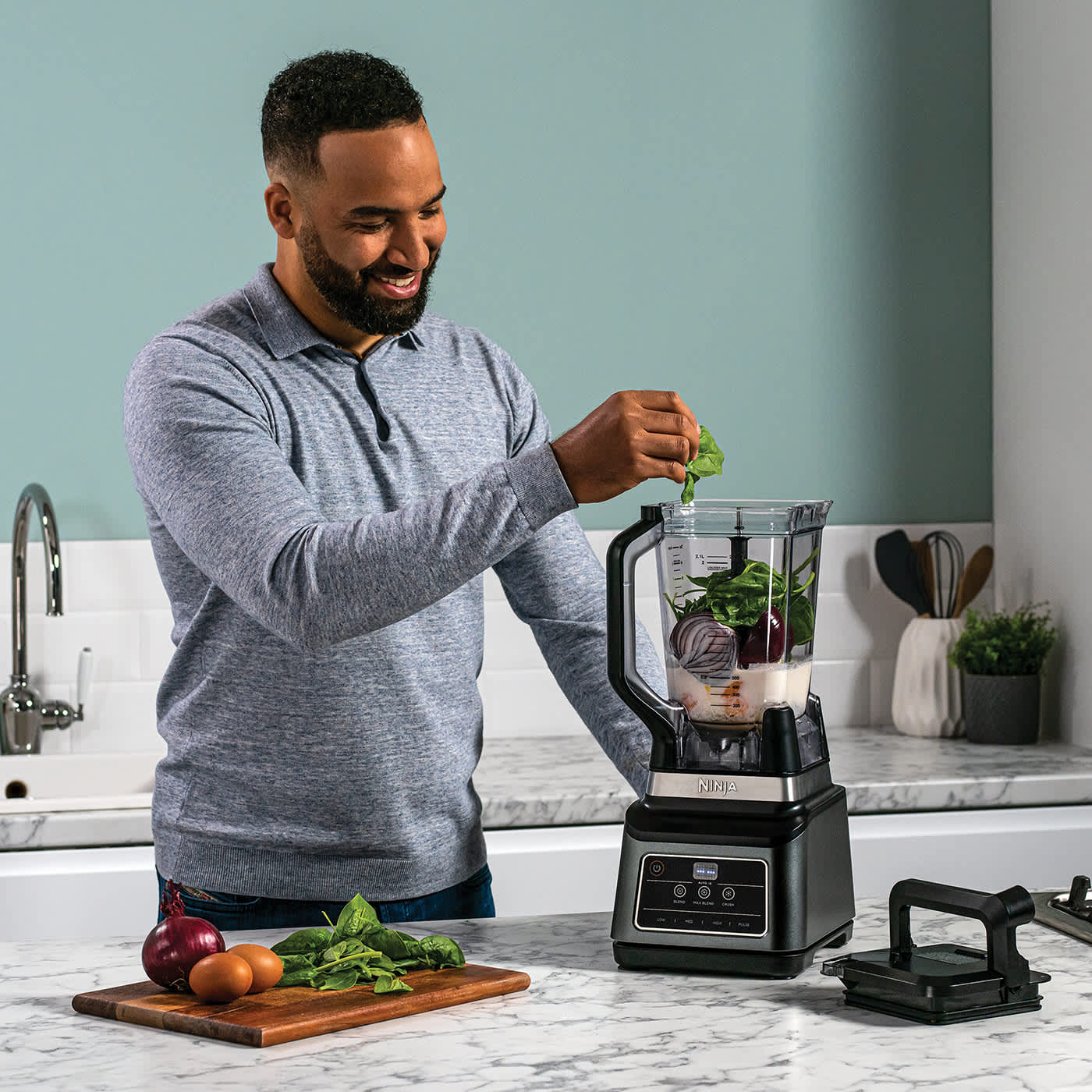 Homme ajoutant des l&eacute;gumes dans le blender Ninja.
