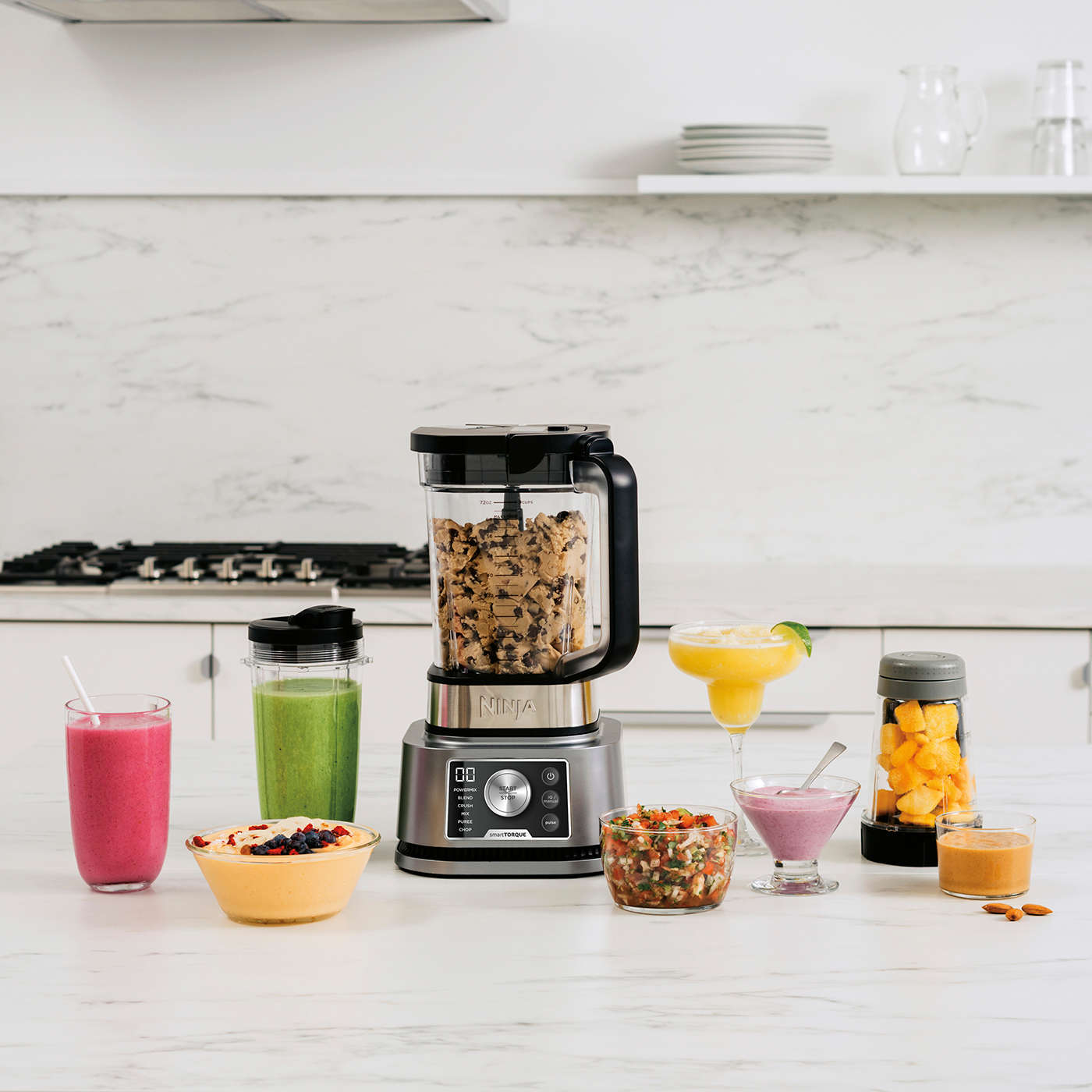 Blender pos&eacute; sur une table, entour&eacute; de boissons et de plats pr&eacute;par&eacute;s avec l&rsquo;appareil.