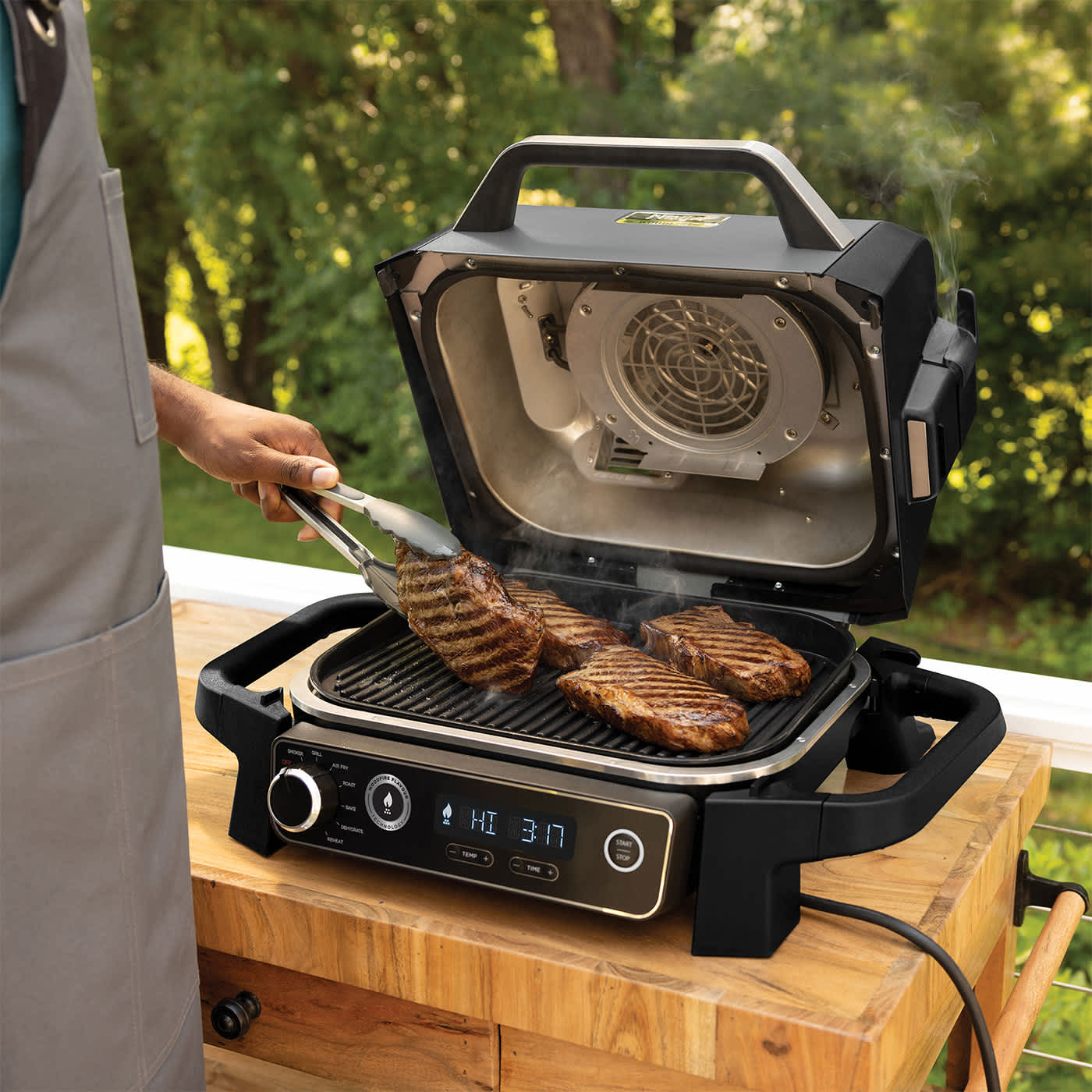 Personne utilisant des pinces pour cuire des steaks sur le barbecue Ninja OG701EU.