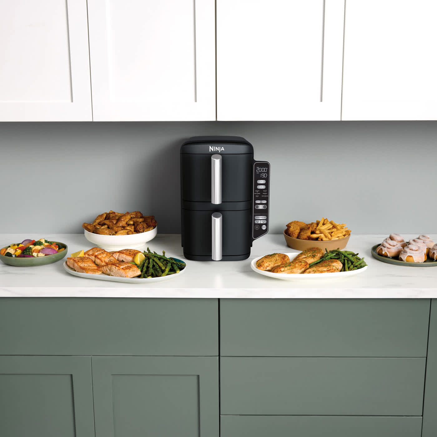 Airfryer pos&eacute; sur un plan de travail, entour&eacute; de plusieurs assiettes de nourriture.