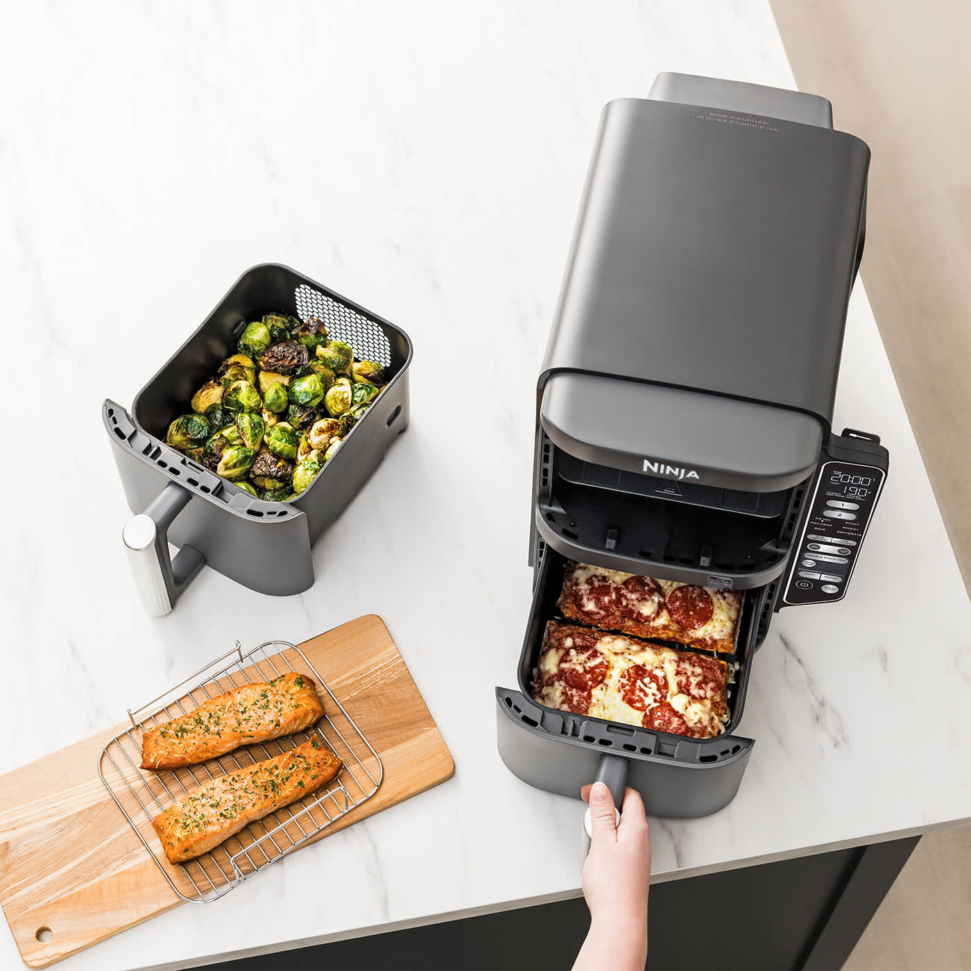 Personne cuisinant une pizza dans un tiroir de l'air fryer Ninja avec l'autre tiroir contenant des l&eacute;gumes.
