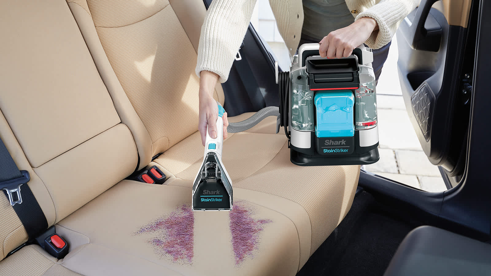 Personne retirant des taches d'un tissu d'ameublement de voiture avec le d&eacute;tacheur Shark.