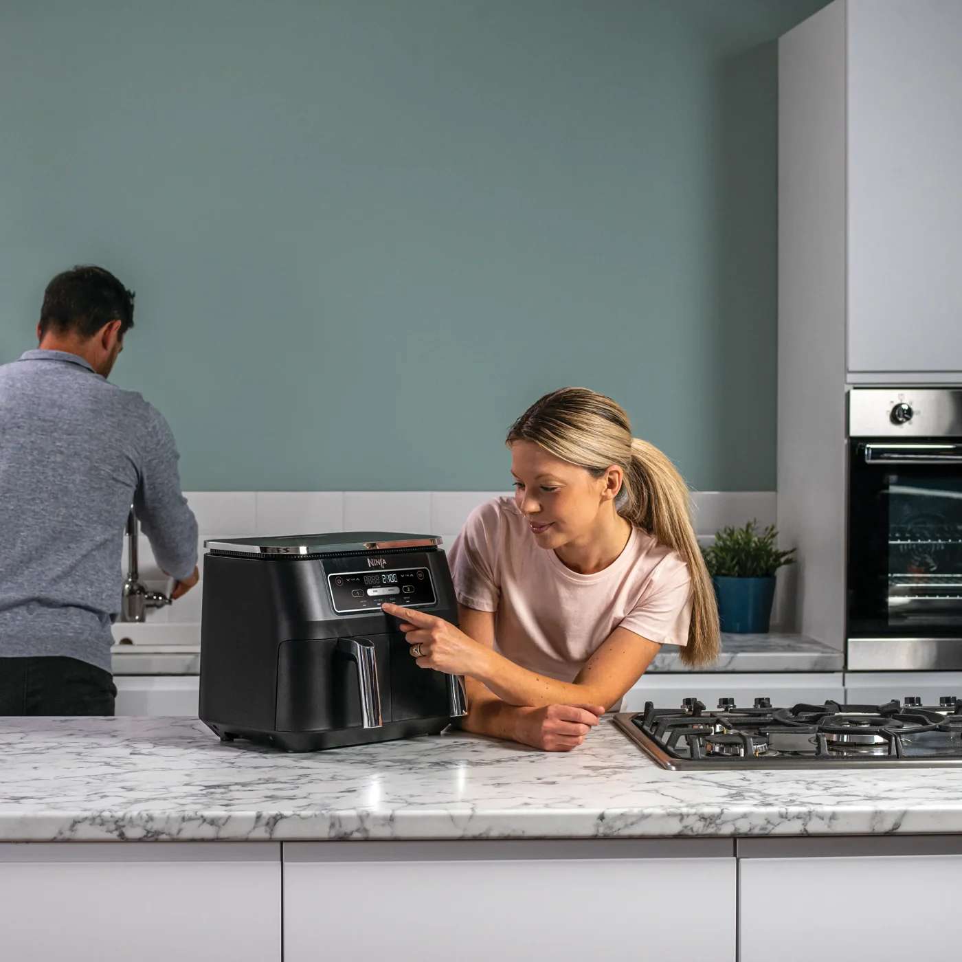 Person bedient den Dual-Zone Ninja Air Fryer &uuml;ber das Bedienfeld.