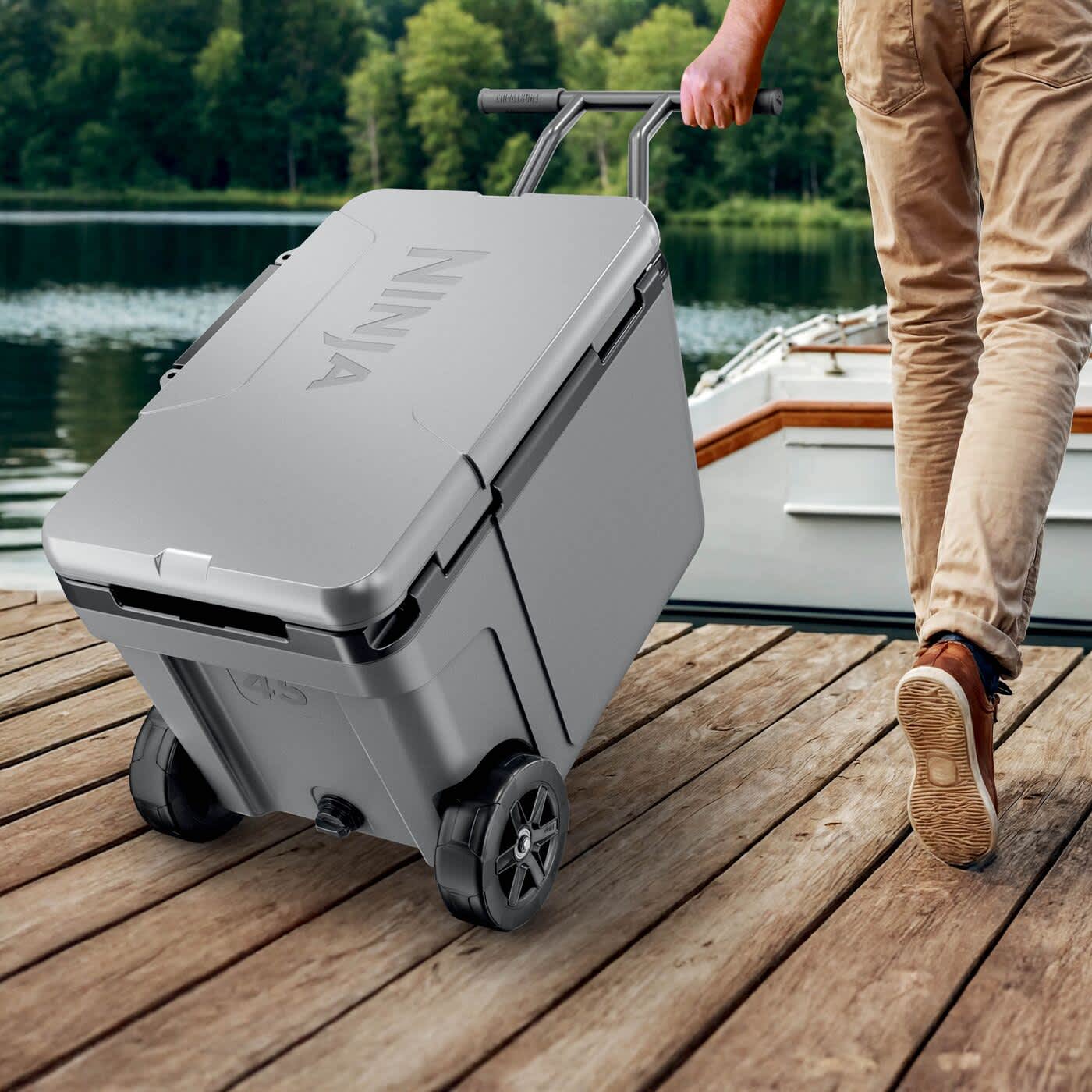 Person rollt die Ninja FrostVault K&uuml;hlbox zum Boot im Freien f&uuml;r Outdoor- und Angelabenteuer