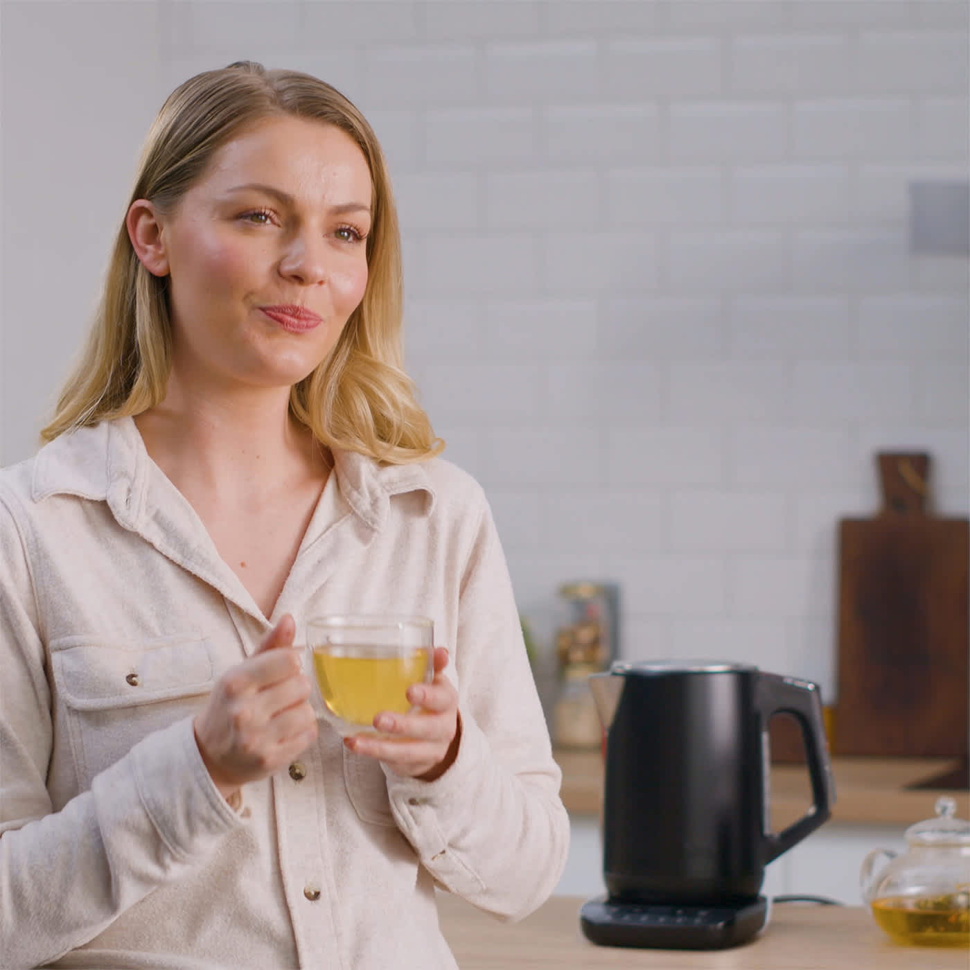 Person h&auml;lt Tasse mit einem warmen Getr&auml;nk in der Hand und dahinter steht der Ninja Wasserkocher KT200EU