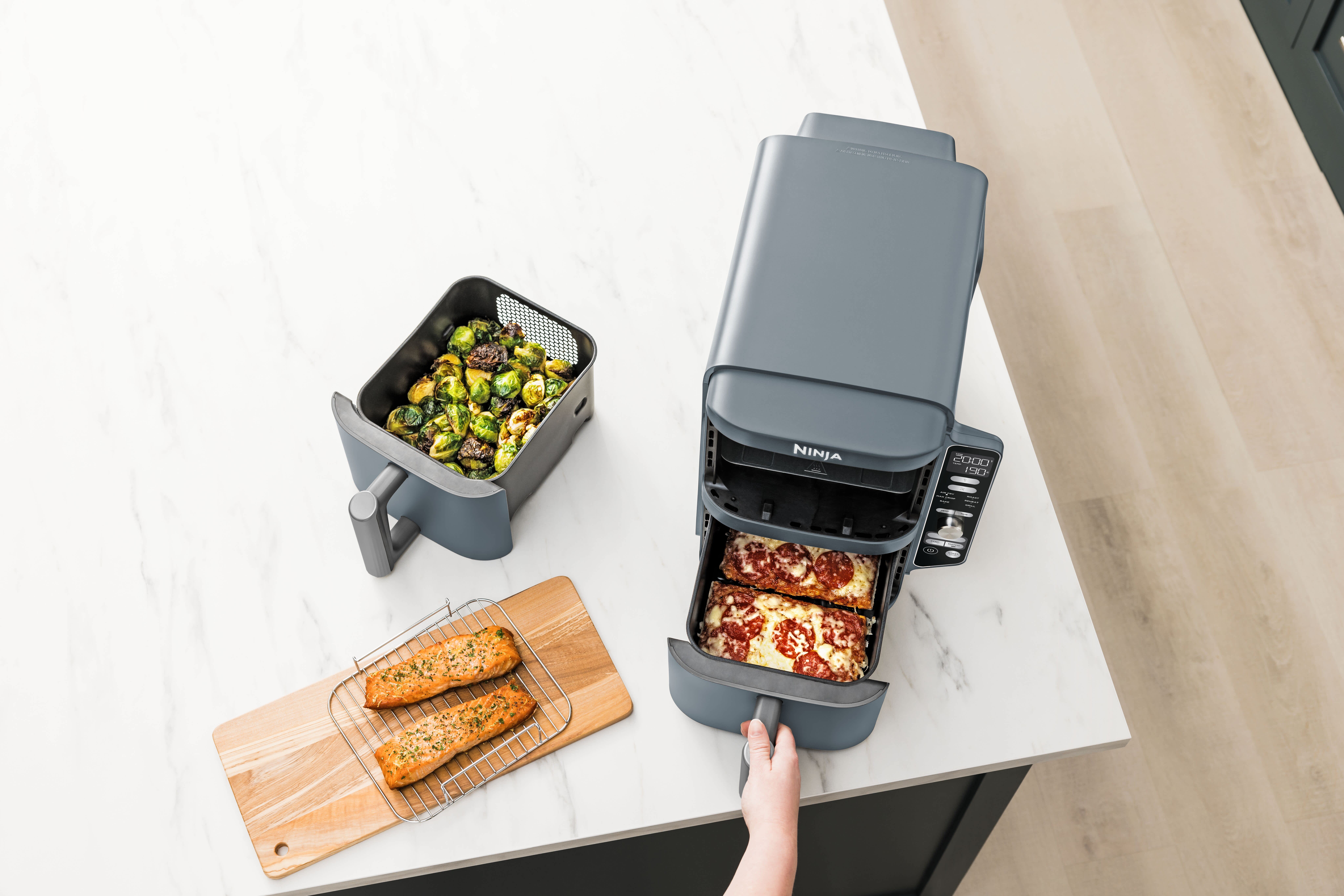 Personne cuisinant une pizza dans un tiroir de l'air fryer Ninja avec l'autre tiroir contenant des l&eacute;gumes.