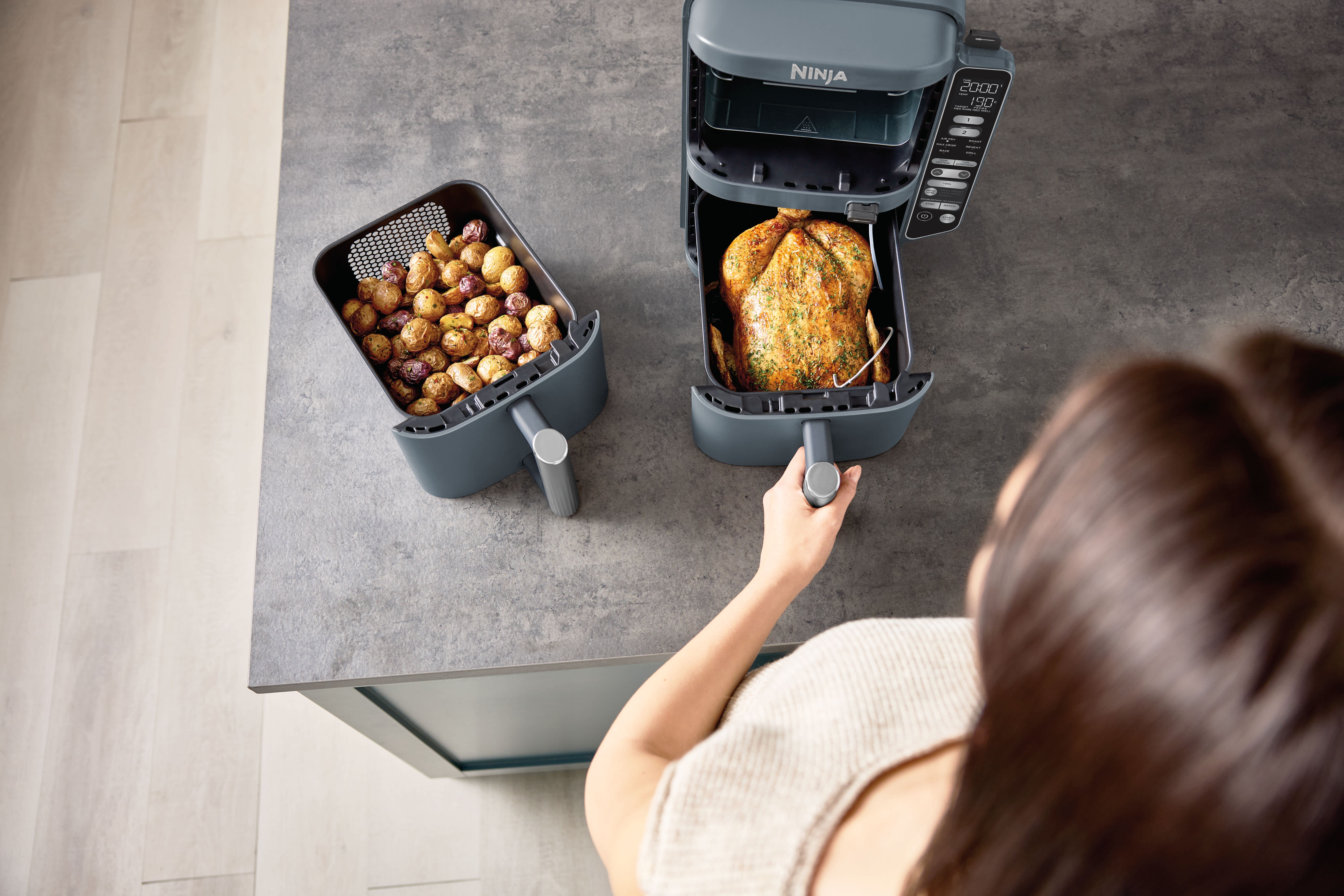 Femme tirant le tiroir du Ninja DoubleStack contenant un poulet frit avec une thermosonde plant&eacute;e avec &agrave; c&ocirc;t&eacute; le deuxi&egrave;me tiroir contenant des pommes de terre grenaille