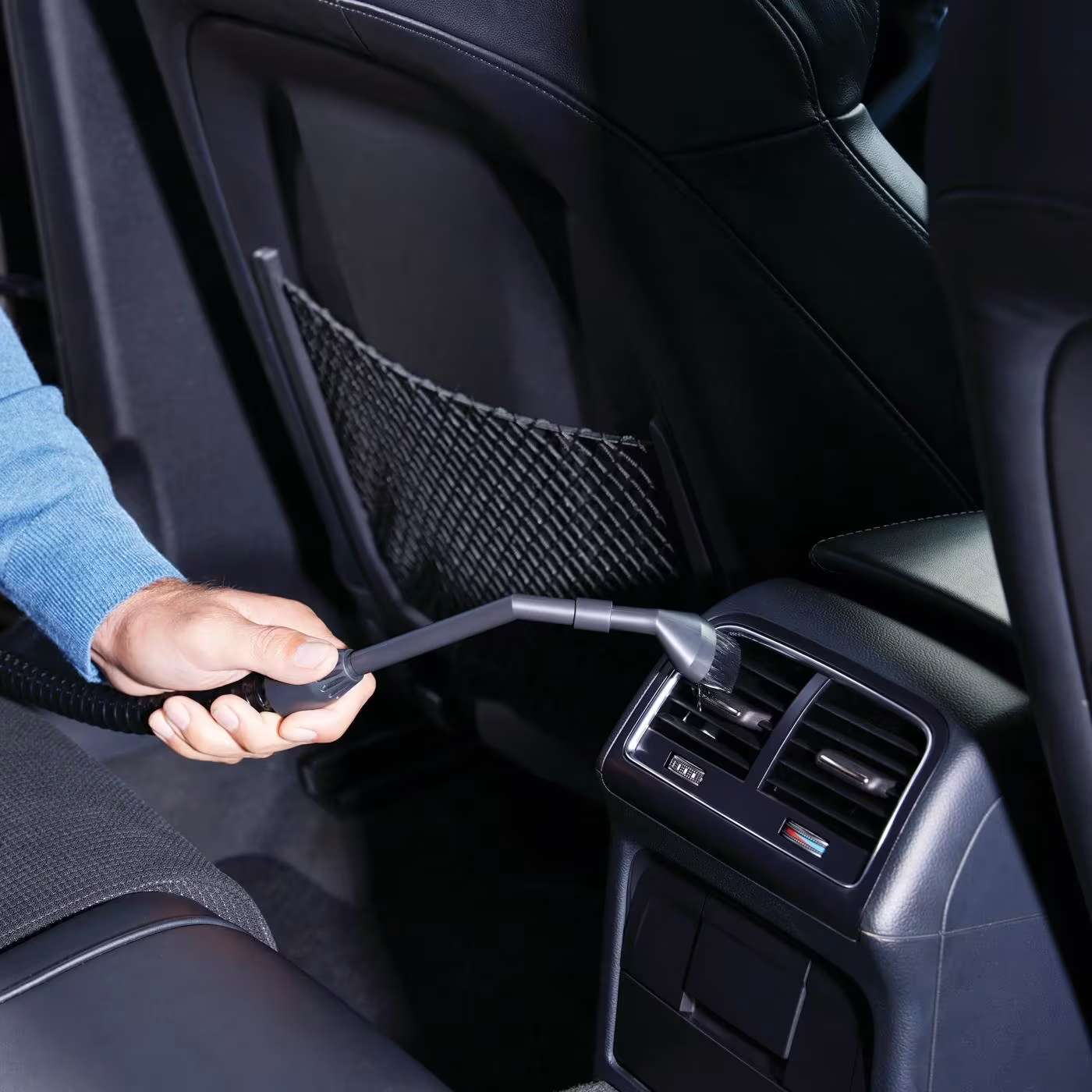 Person reinigt die Mittelkonsole eines Autos mit dem Handsauger.