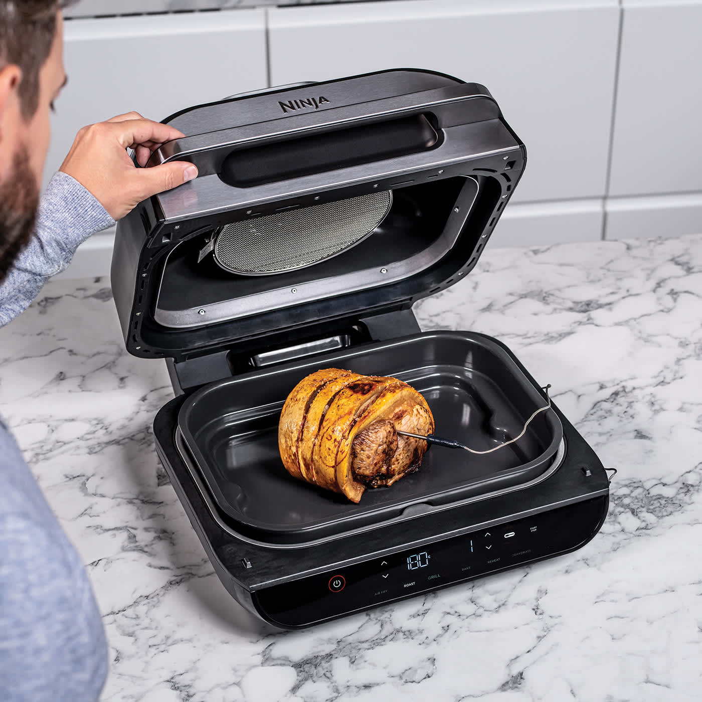 Eine Person grillt bei offenem Ninja Foodi MAX 6-in-1 Grill Fleisch.