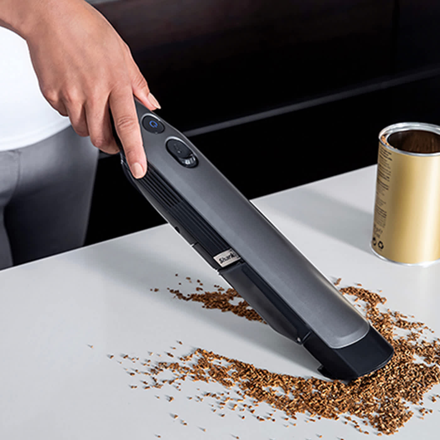 Kabelloser Handstaubsauger saugt Kaffeepulver von wei&szlig;er Tischfl&auml;che &ndash; Anwendung im Haushalt