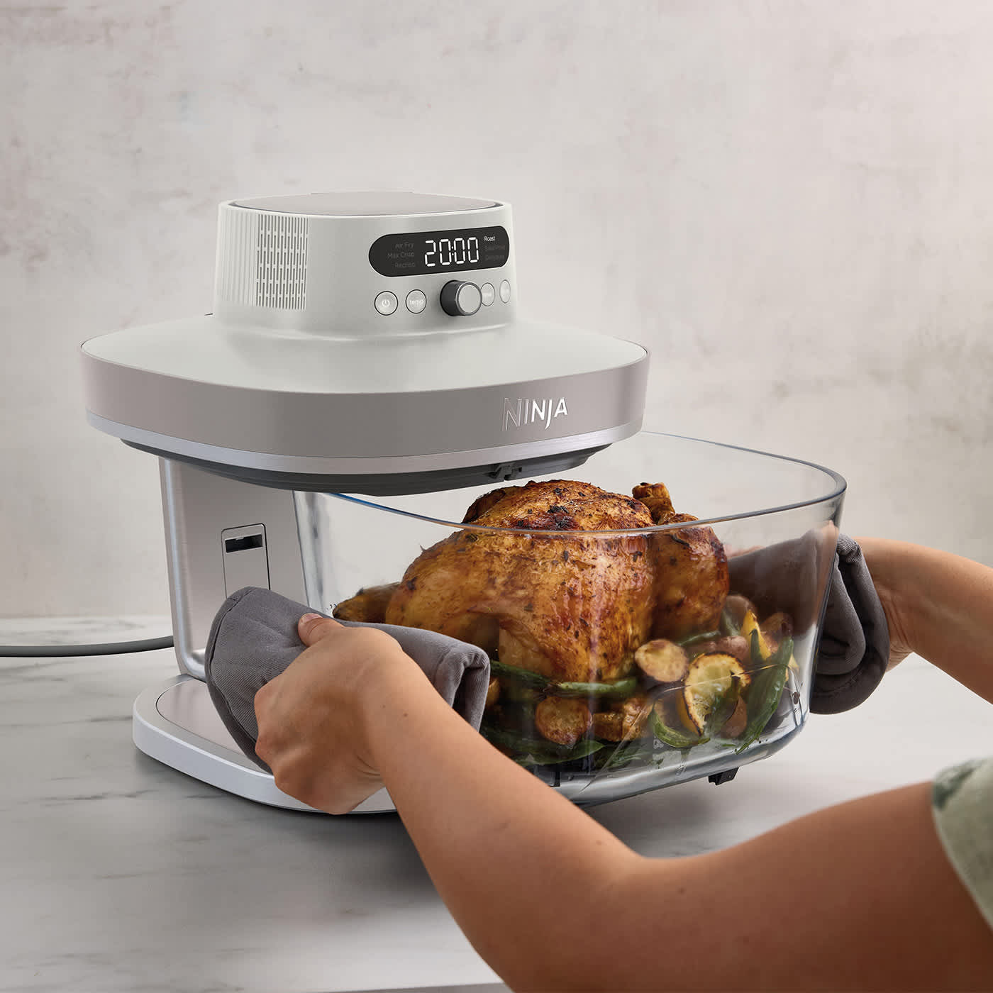 Persona che inserisce il contenitore grande con dentro un pollo nella Friggitrice ad aria in vetro Ninja CRISPi PRO