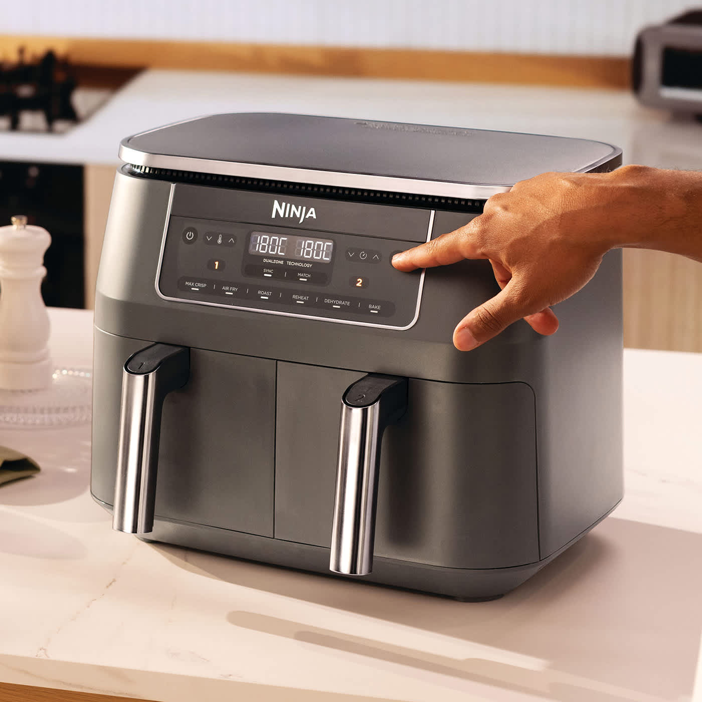Friggitrice ad aria Ninja Dual Zone da 7,6 L con una mano che preme uno dei suoi pulsanti