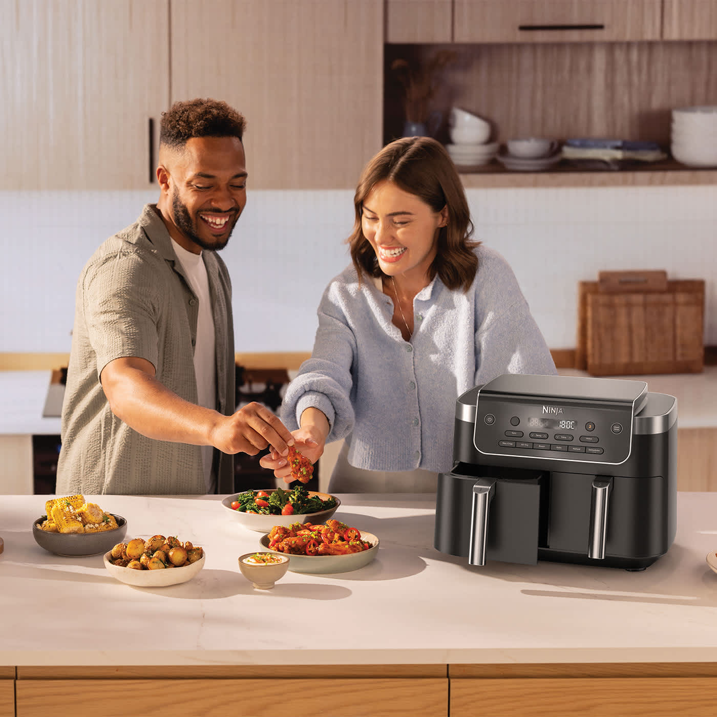 Immagine di un uomo e una donna con la Friggitrice ad aria Ninja Dual Zone da 7,6 L e diversi piatti preparati