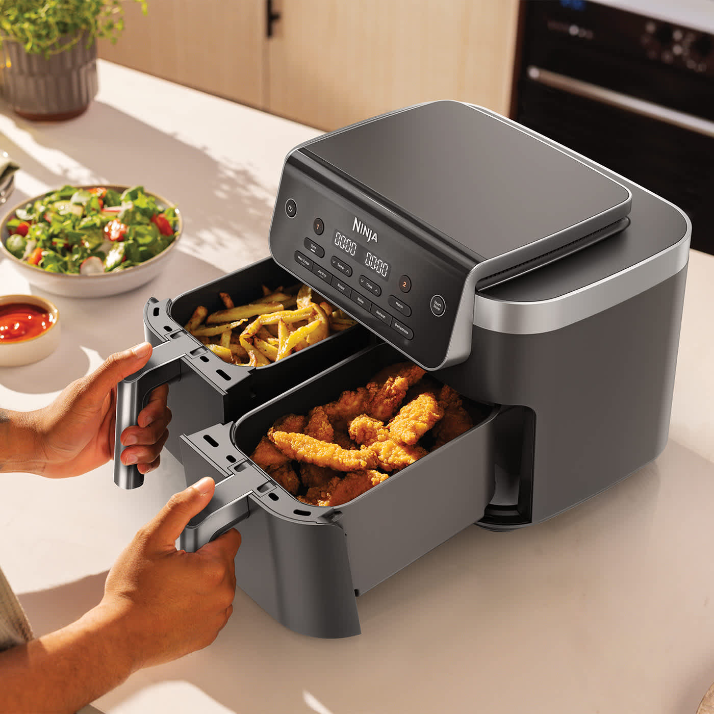 Personne ouvrant les deux tiroirs de l'air fryer, l'un contenant du poulet et l'autre des frites.