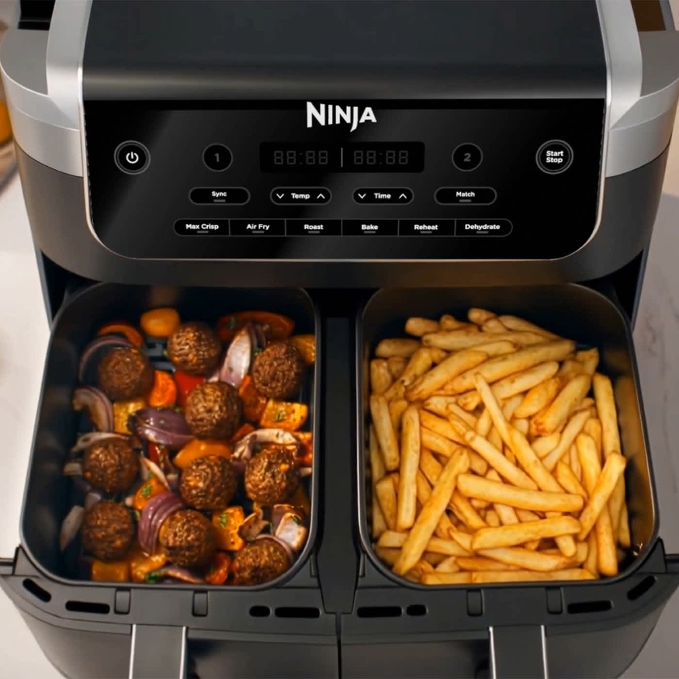 Friggitrice ad aria Ninja Dual Zone da 7,6 L con i cassetti aperti con dentro patatine fritte in uno e polpette nell'altro