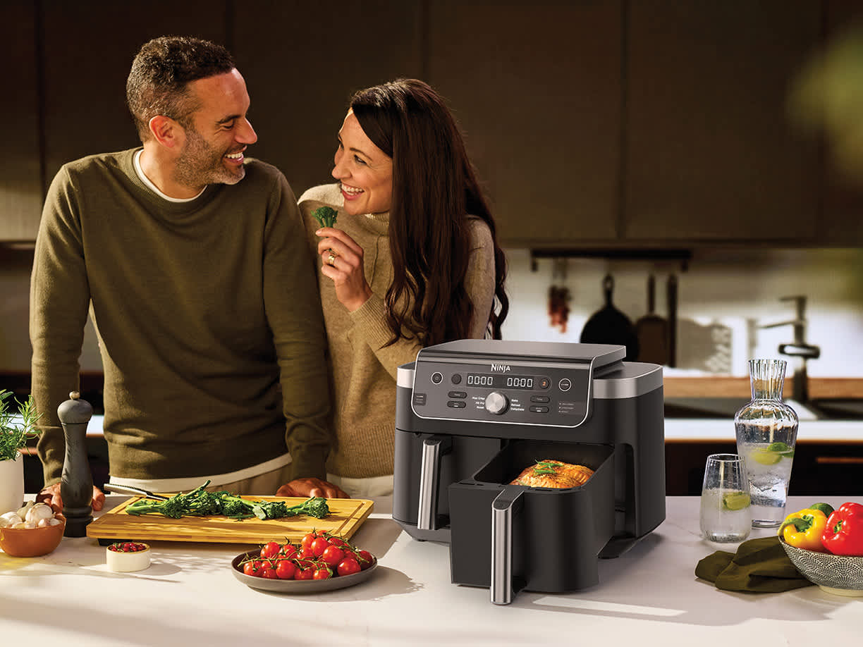 Immagine di un uomo e una donna in cucina con la Friggitrice ad aria Ninja Dual Zone da 9,5 L su un piano di lavoro con ingredienti