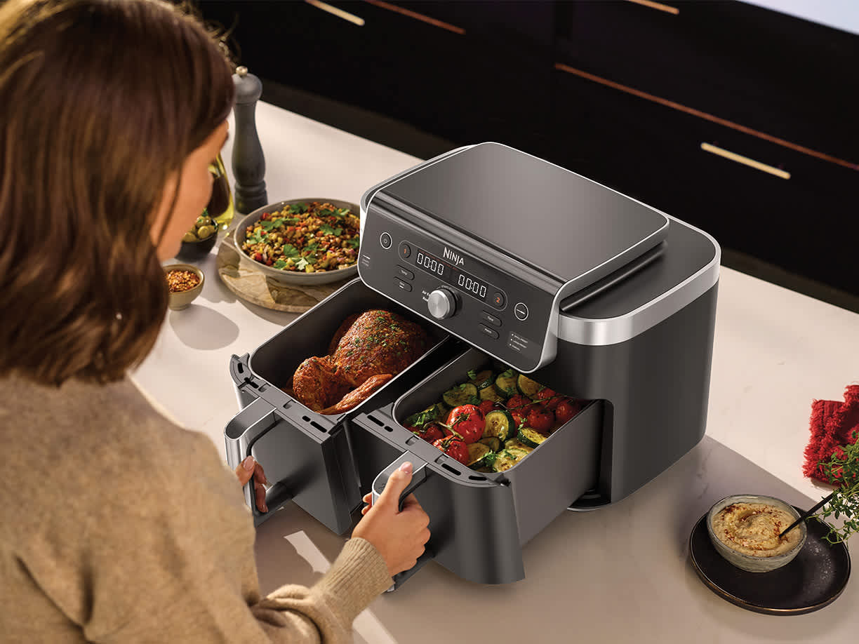 Friggitrice ad aria Ninja Dual Zone da 9,5 L con i cassetti aperti con un pollo dentro uno e verdure dentro l'altro