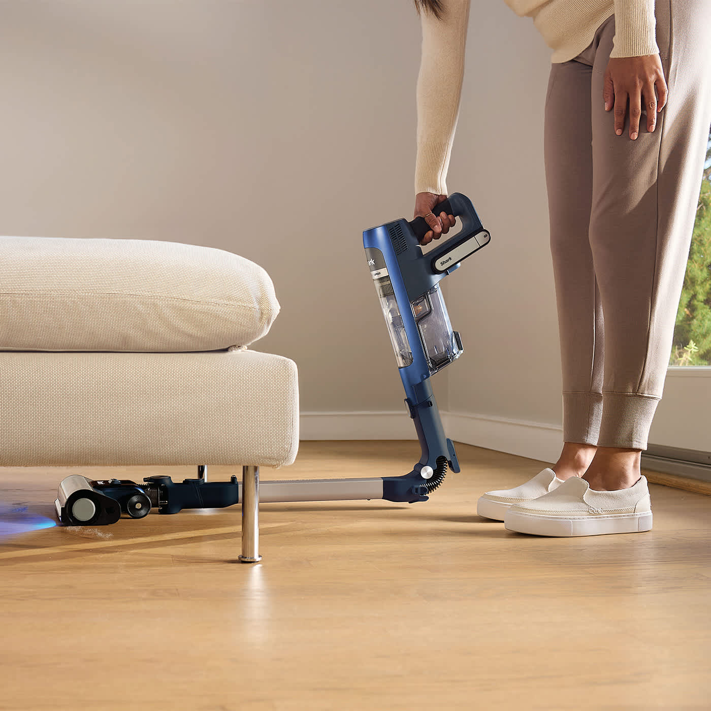 Personne utilisant la fonction Flex de l&rsquo;aspirateur sans fil Shark pour aspirer sous une chaise.