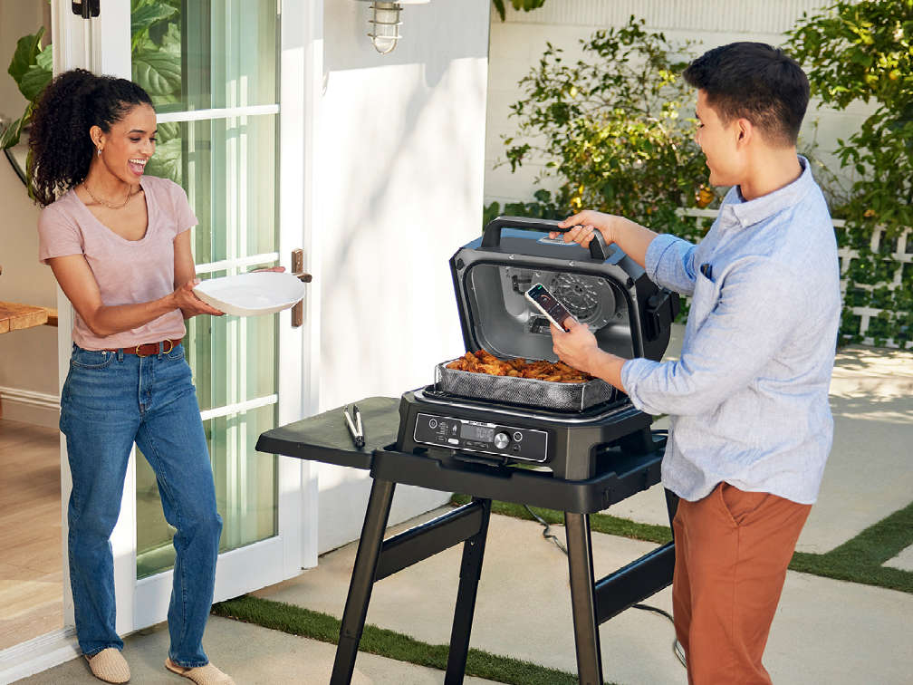 Immagine di due persone all'aperto che usano il barbecue elettrico Ninja Woodfire XL