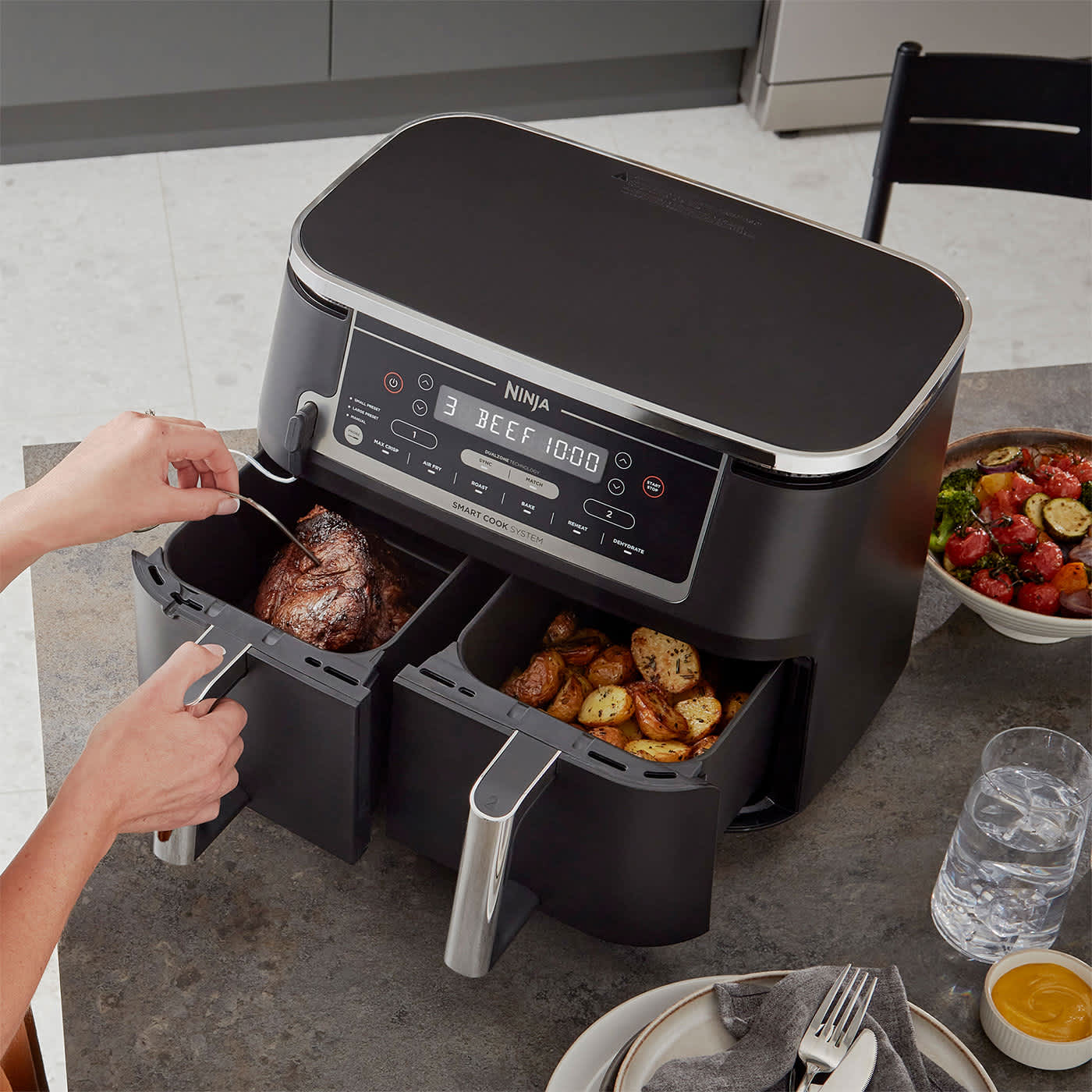Air Fryer Ninja AF451EU stojący na stole z dwoma r&oacute;żnymi potrawami w oddzielnych szufladach upieczonych jednocześnie