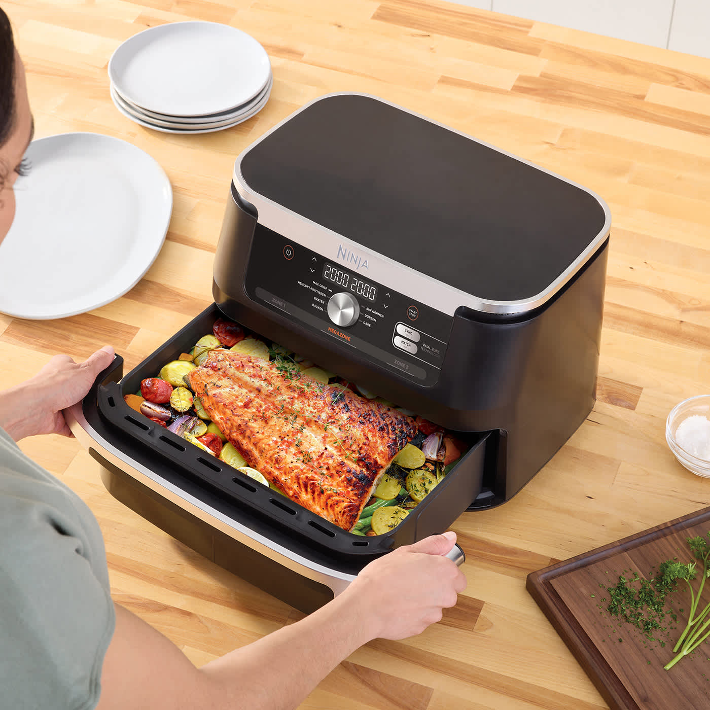 Kobieta wysuwająca szufladę z gotowymi potrawami z air fryera Ninja Foodi FlexDrawer 10,4 l AF500EU stojącego na stole