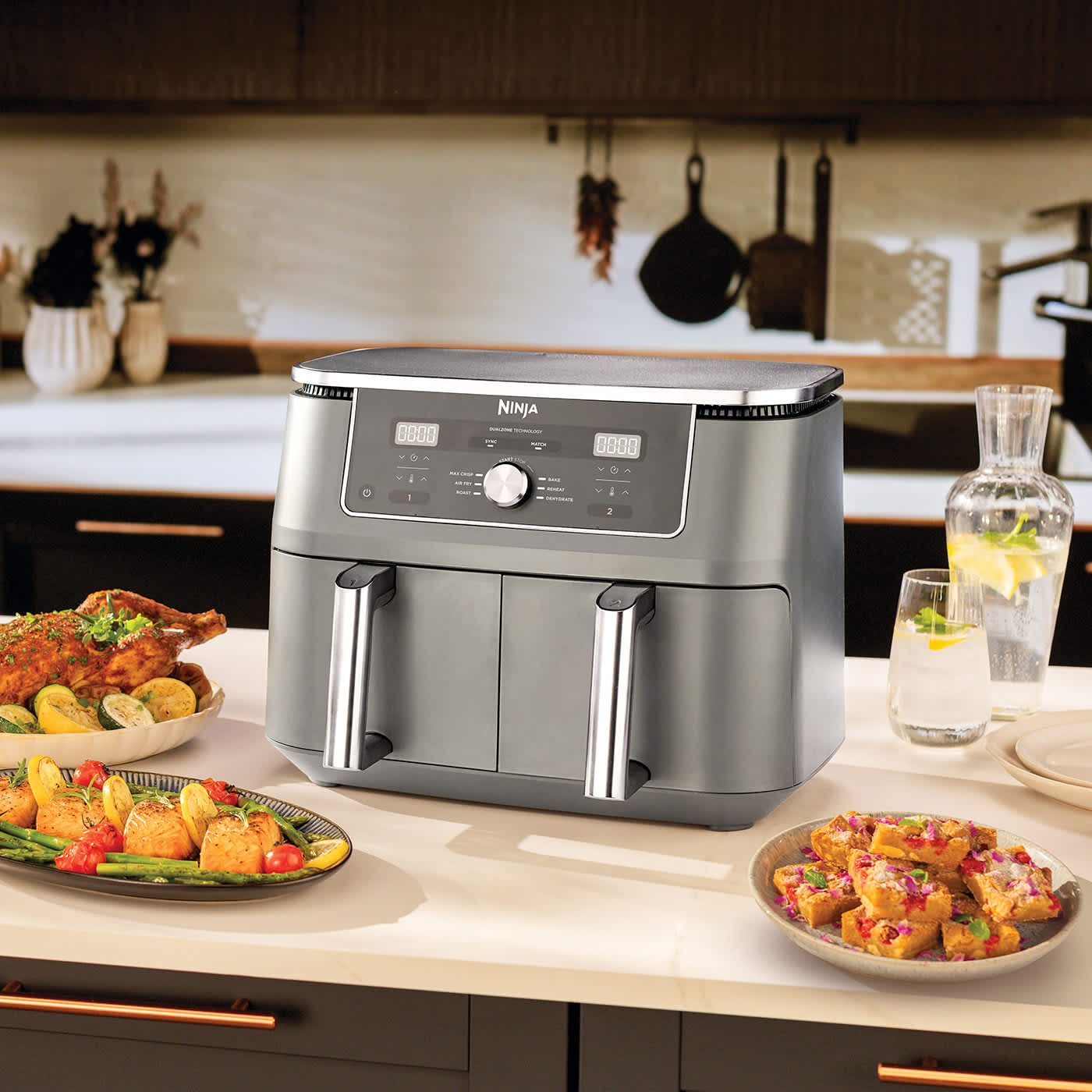 Air fryer Ninja MAX 6-in-1 Dual Zone 9,5 l DZ400EU stojący na blacie kuchennym w otoczeniu wielu przygotowanych w nim potraw