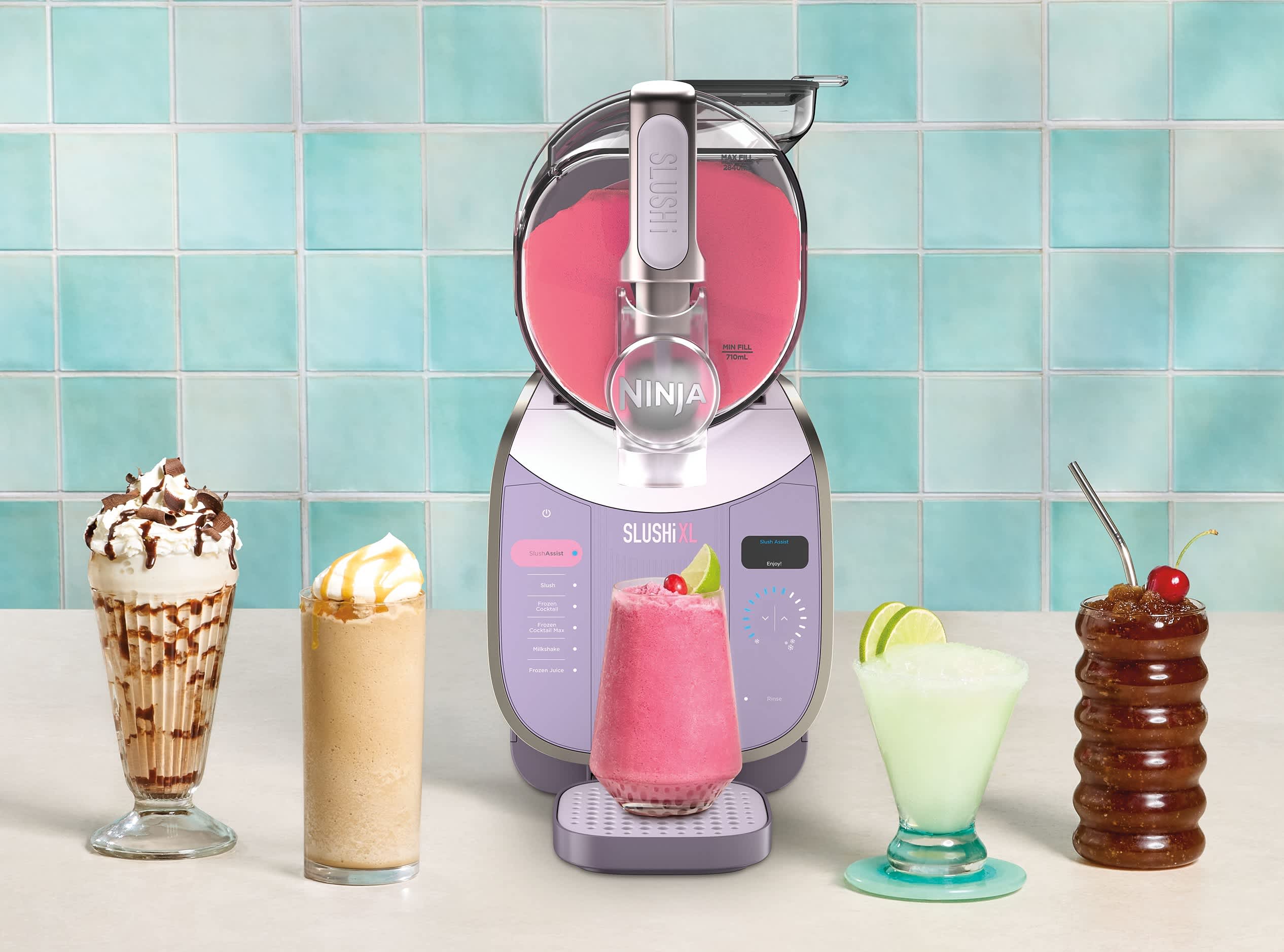 Maszynka do mrożonych napoj&oacute;w i slushy Ninja Slushi XL FS601EU stojąca na blacie w kuchni w otoczeniu wielu r&oacute;żnokolorowych mrożonych koktajli przygotowanych z jej udziałem