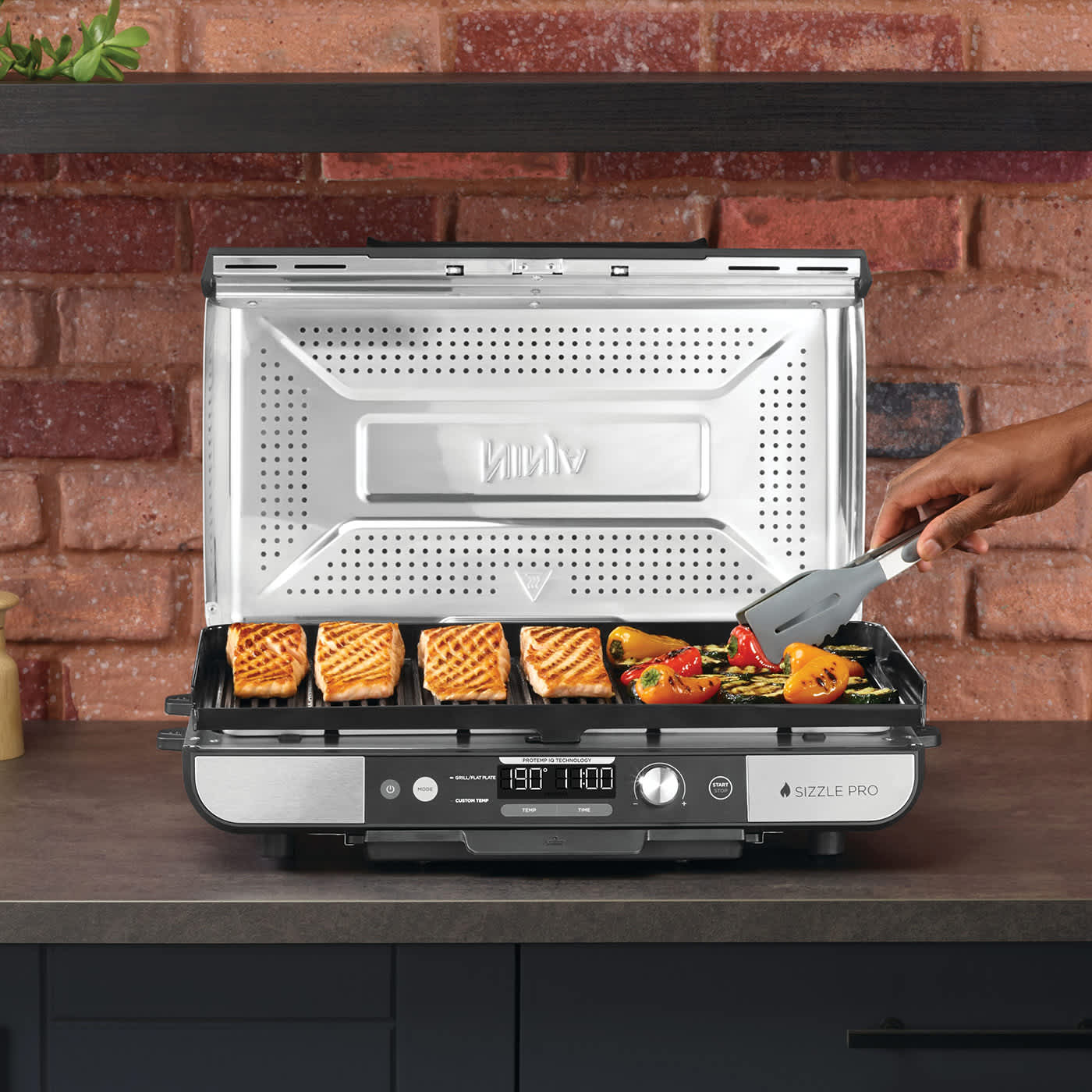 Osoba przekłada na drugą stronę grillowane produkty na Ninja Sizzle PRO XL Grill+Plancha GX101EU