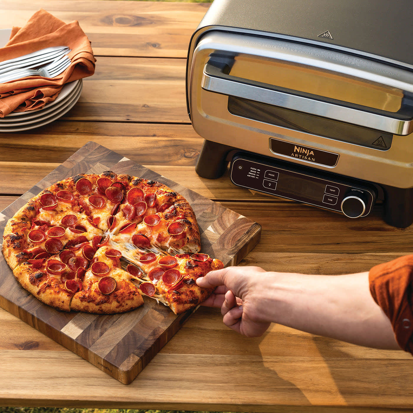 Osoba częstuje się kawałkiem pizzy upieczonej w elektrycznym zewnętrznym piecu do pizzy i air fryerze Ninja Artisan MO201EU