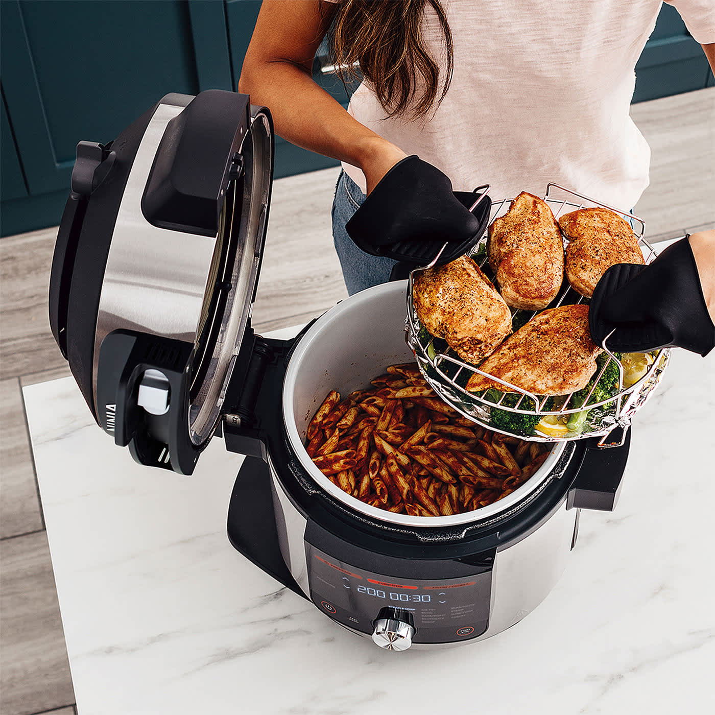 Kobieta wyciąga upieczone piersi z kurczaka z multicookera Ninja Foodie MAX SmartLid 14 w 1 OL750EU