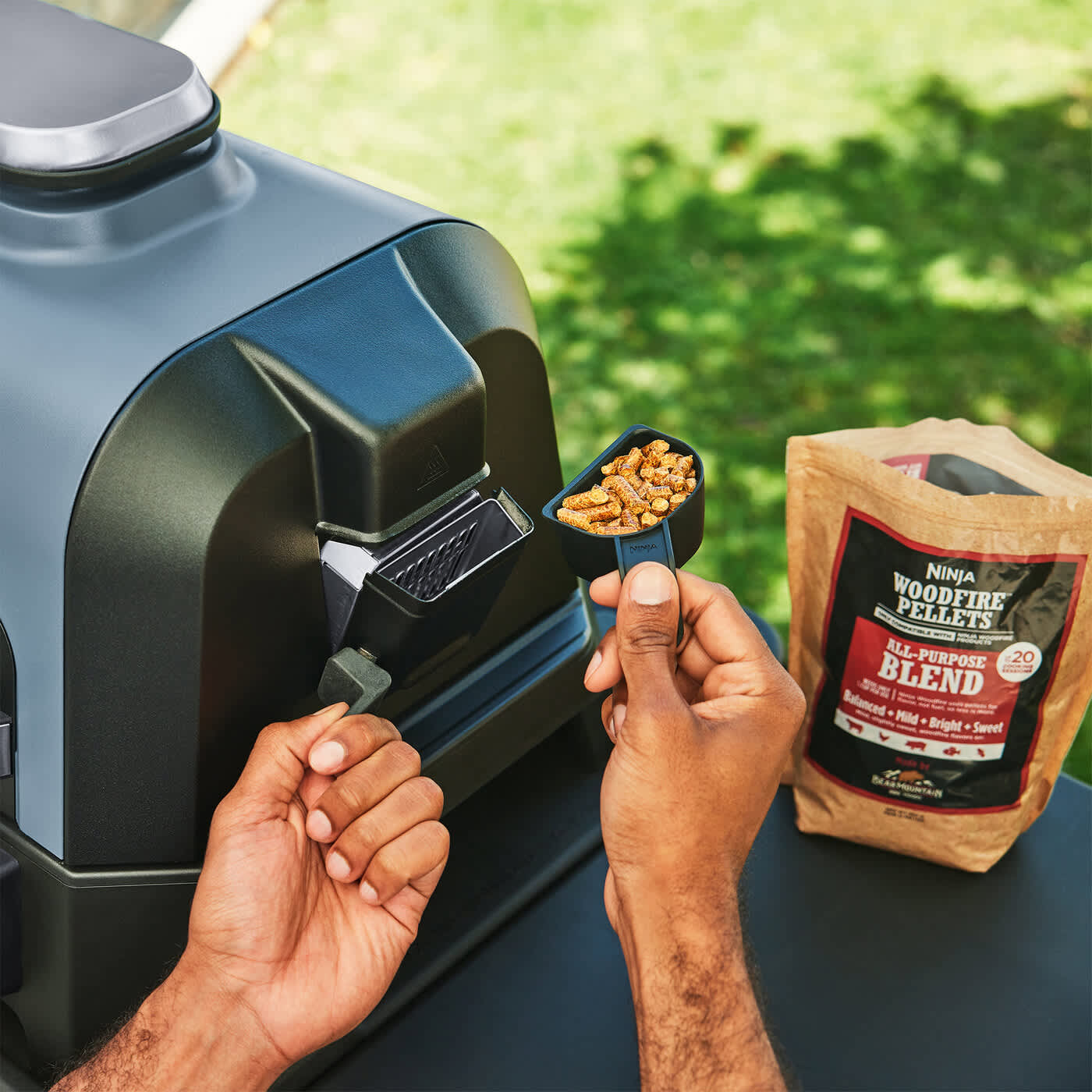 Personne ajoutant des granul&eacute;s de bois dans le barbecue Ninja.