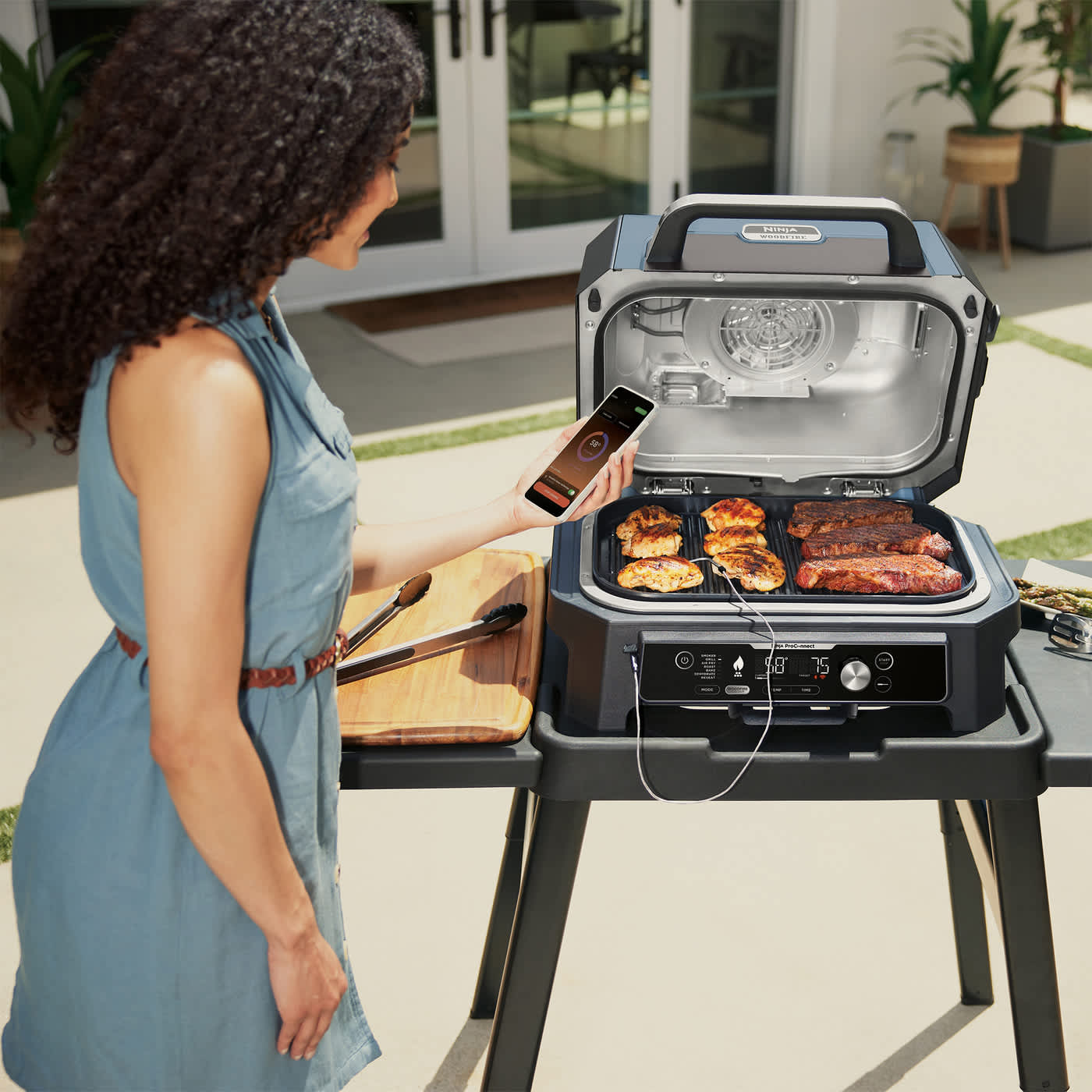 Femme cuisant de la viande sur un barbecue Ninja, en utilisant une application mobile pour contr&ocirc;ler la temp&eacute;rature.