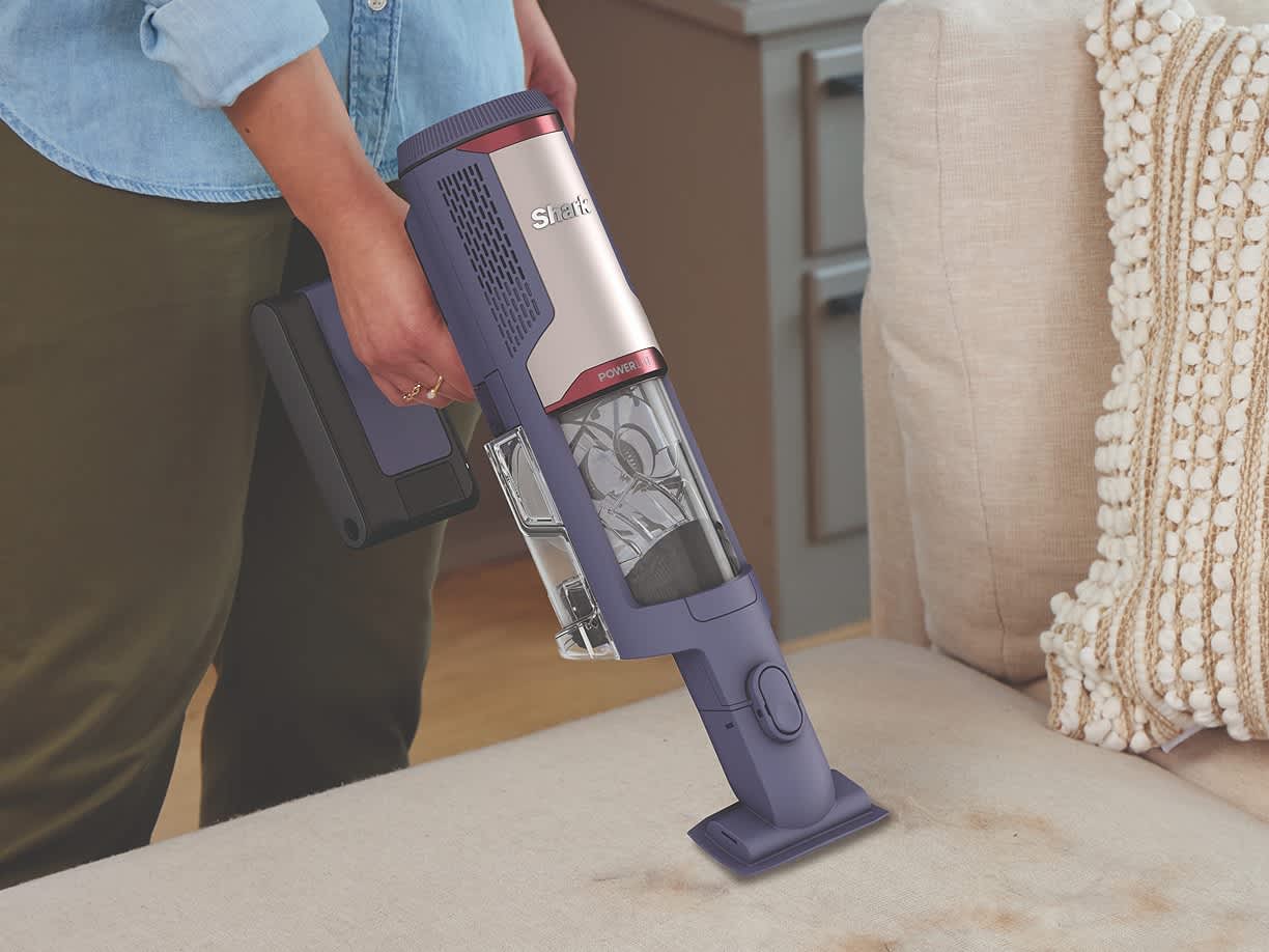Kobieta odkurza kanapę odkurzaczem bezprzewodowym Shark PowerLite Clean & Empty Pet w trybie odkurzacza ręcznego