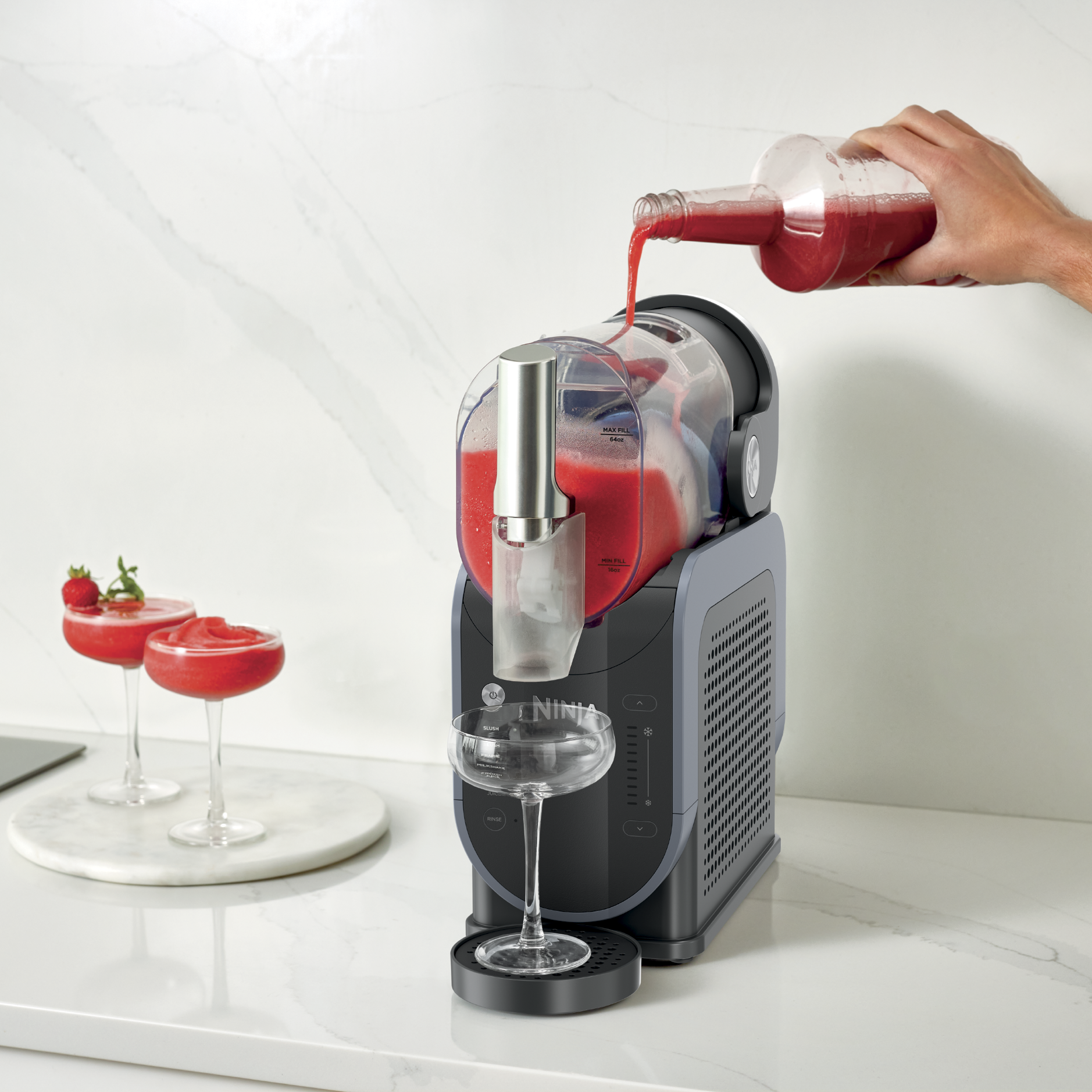 Personne versant du jus dans la machine &agrave; slush, avec deux verres de slush sur le c&ocirc;t&eacute; gauche.