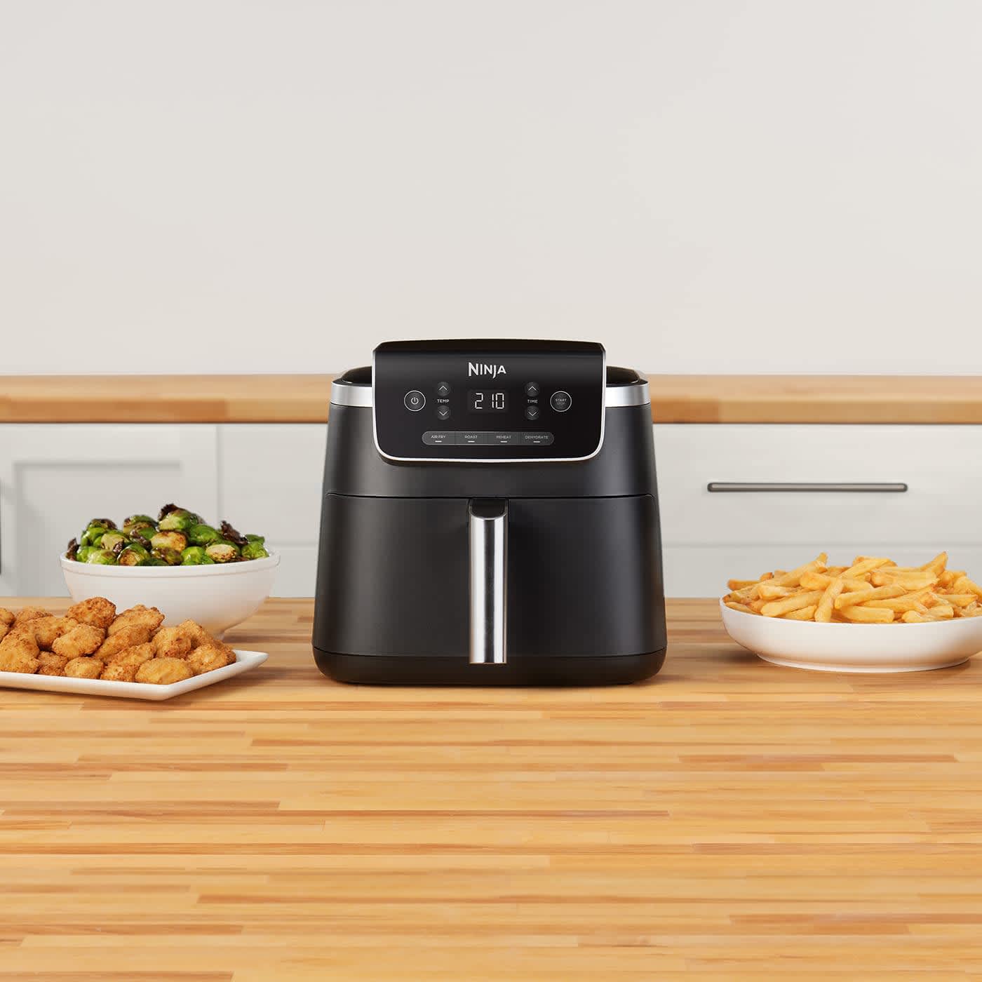 Airfryer entour&eacute; de plusieurs assiettes de l&eacute;gumes, nuggets et frites..