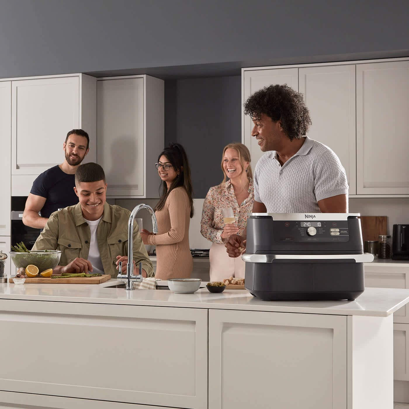 Cinq personnes autour d'un &icirc;lot de cuisine avec le air fryer Ninja sur le comptoir.