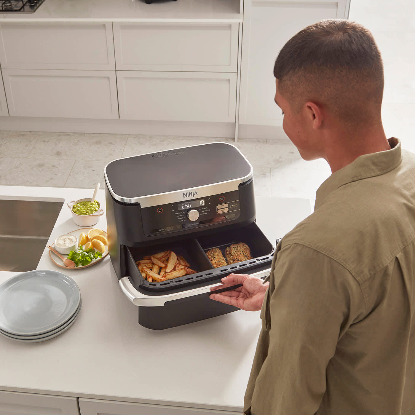 Homme ouvrant le air fryer Ninja AF500EU avec du poisson d'un c&ocirc;t&eacute; et des frites de l'autre.