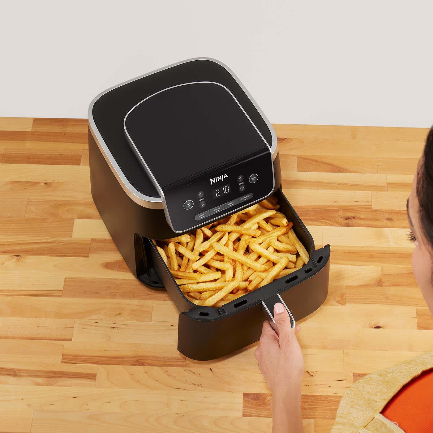Airfryer pos&eacute; sur une table, entour&eacute; de plusieurs assiettes de nourriture, notamment du poisson et un g&acirc;teau.