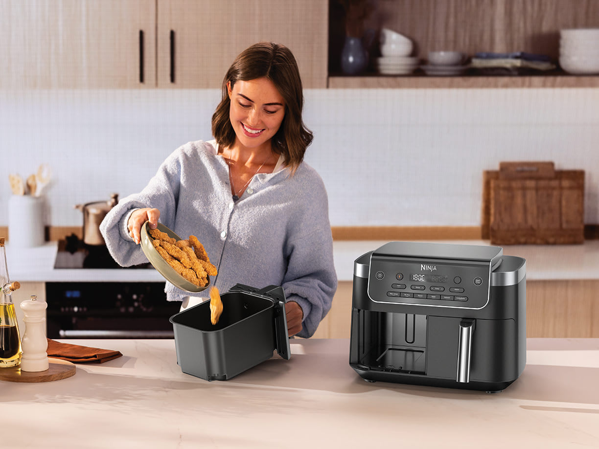Femme versant du poulet frit dans l'air fryer.