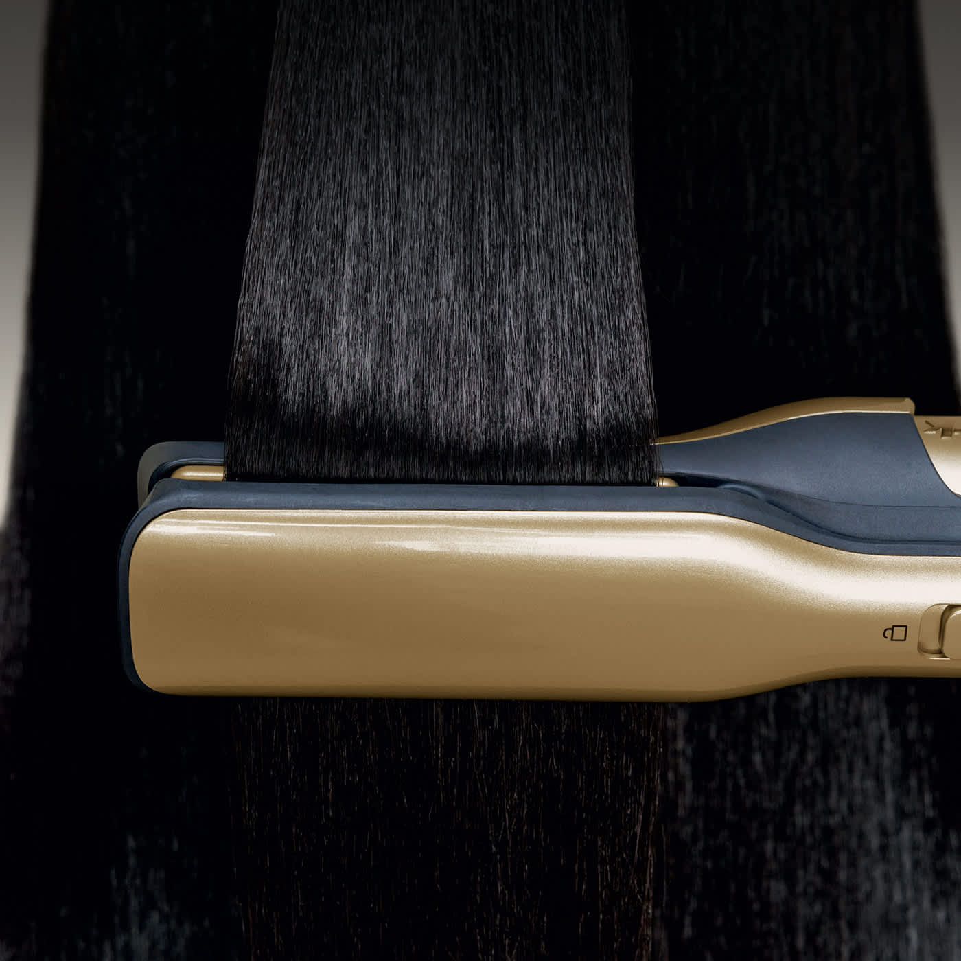 Woman straightens curly hair with a gold flat iron, leaving it smooth and glossy.
