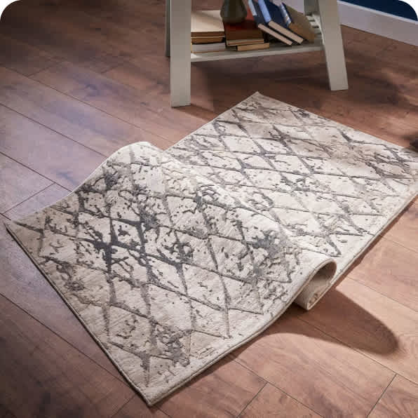 A rug not fully laid out on a wooden floor covered in dirt